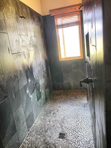 Narrow tiled bathroom with dark walls, shower area, and a bright window at the far end.