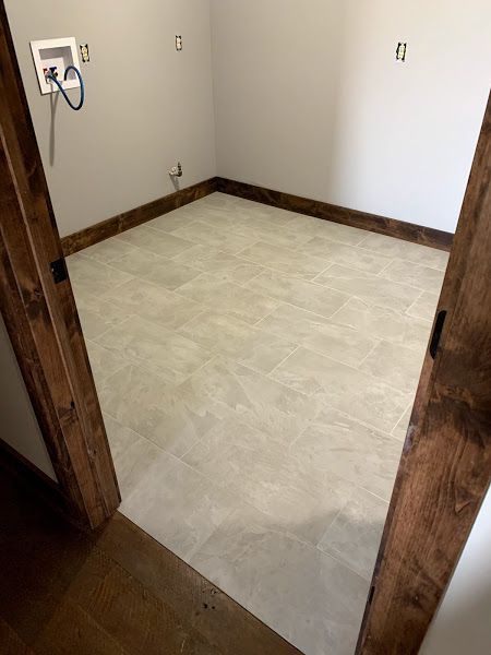 Empty small room with beige tile floor, white walls, and dark wood trim, viewed through an open doorway