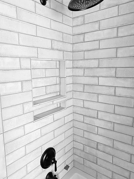 White subway-tiled shower with a small window, black shower head, and chrome grab bars.