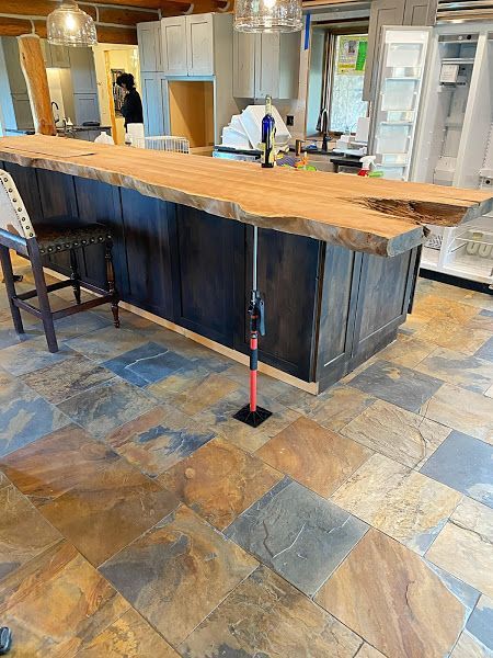 Rustic kitchen with a large wooden island, dark cabinets, and tiled floor under renovation