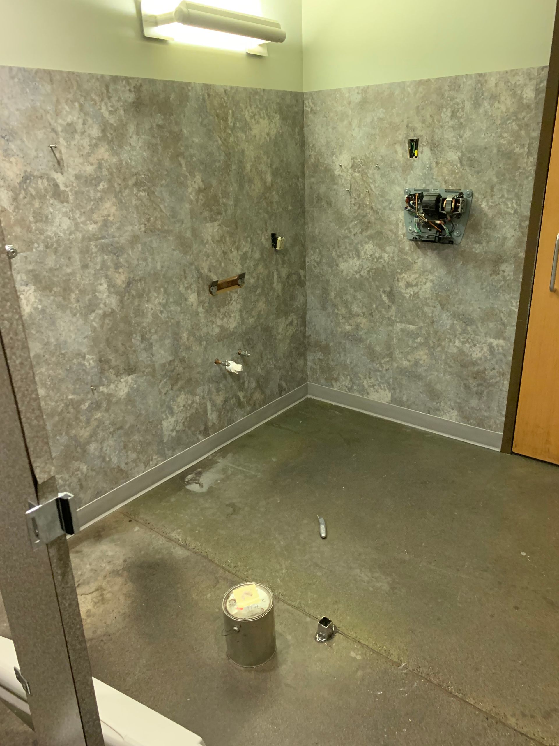 Empty tiled bathroom under construction with exposed plumbing and unfinished gray walls.