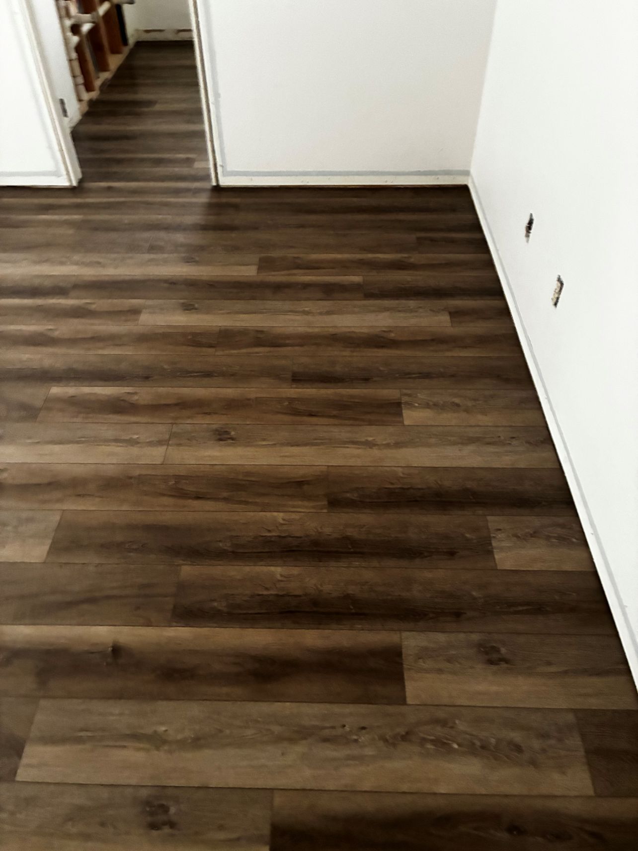Empty room with dark wood flooring and white walls, viewed from a doorway