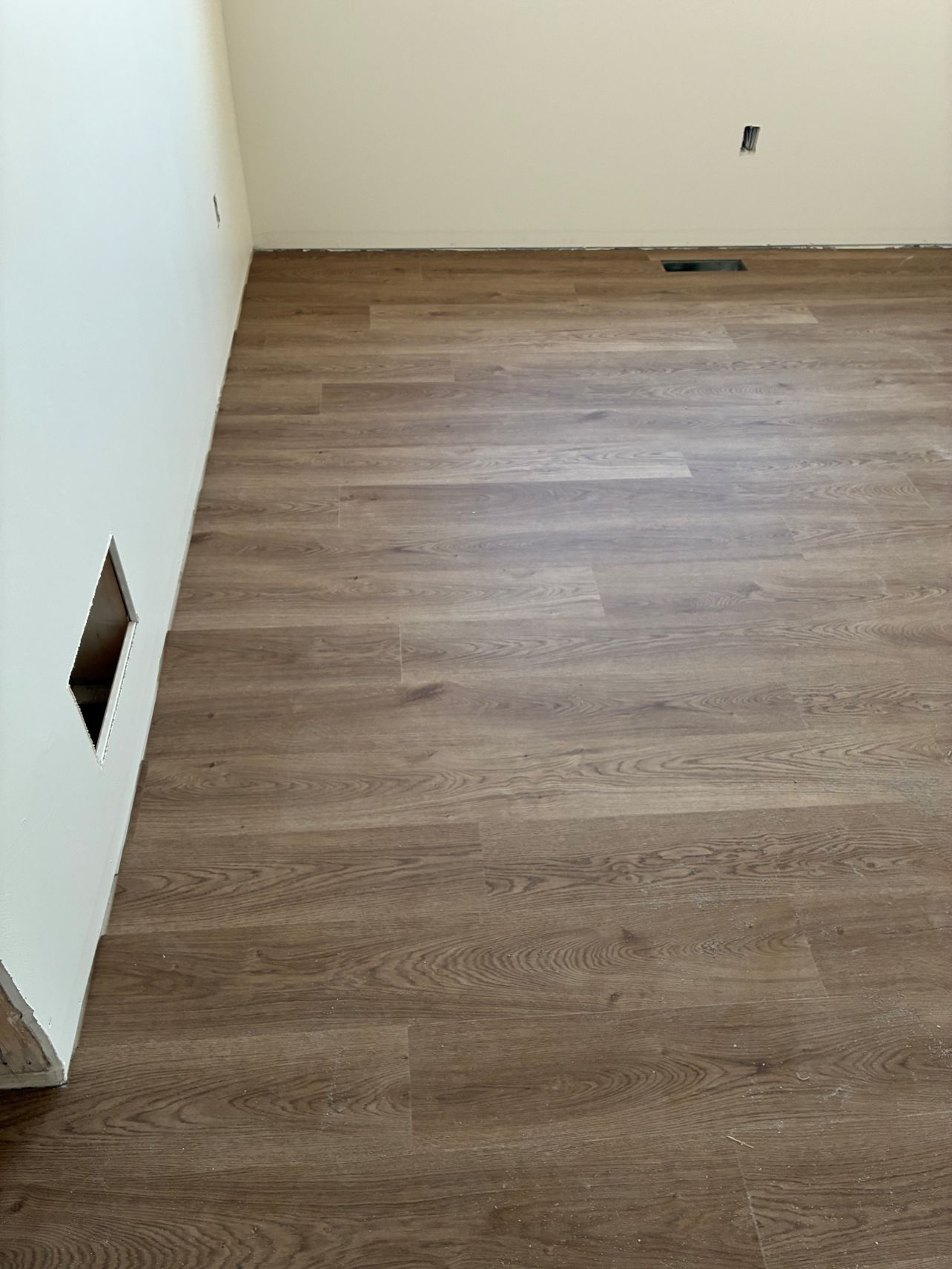Empty room with wood-look flooring and a white wall with wall openings and outlets