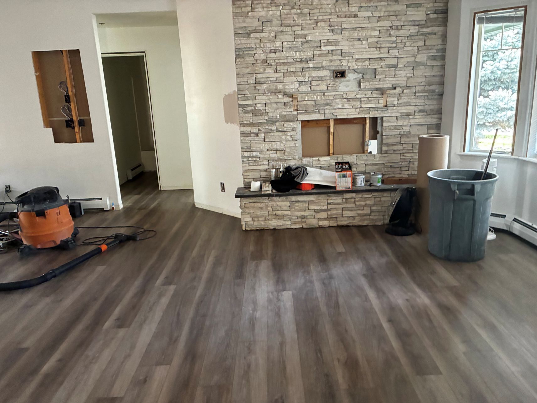 Living room under renovation with stone fireplace, wood flooring, and tools on the floor