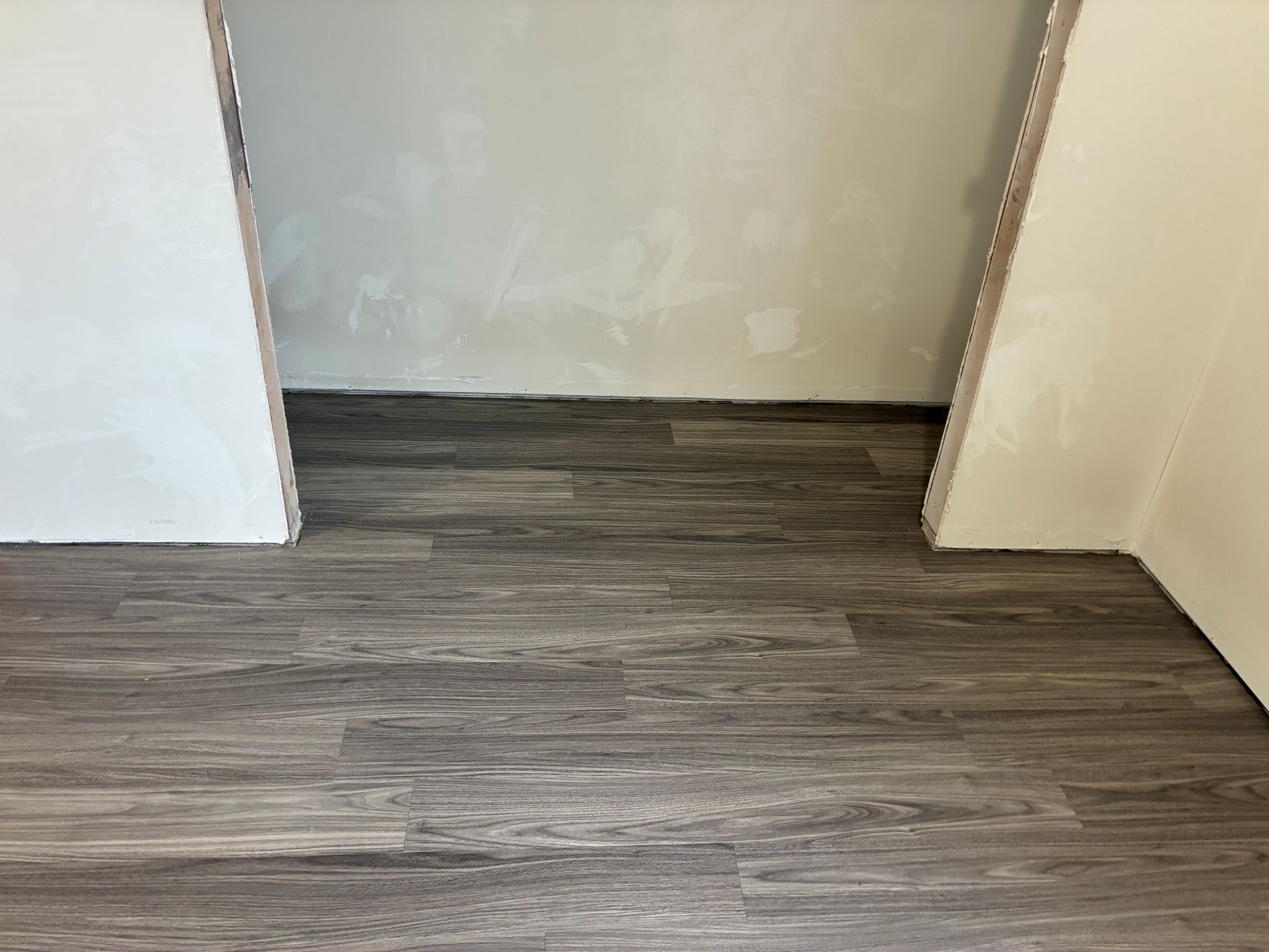 Empty doorway with gray wood-look flooring and white walls in an unfinished room