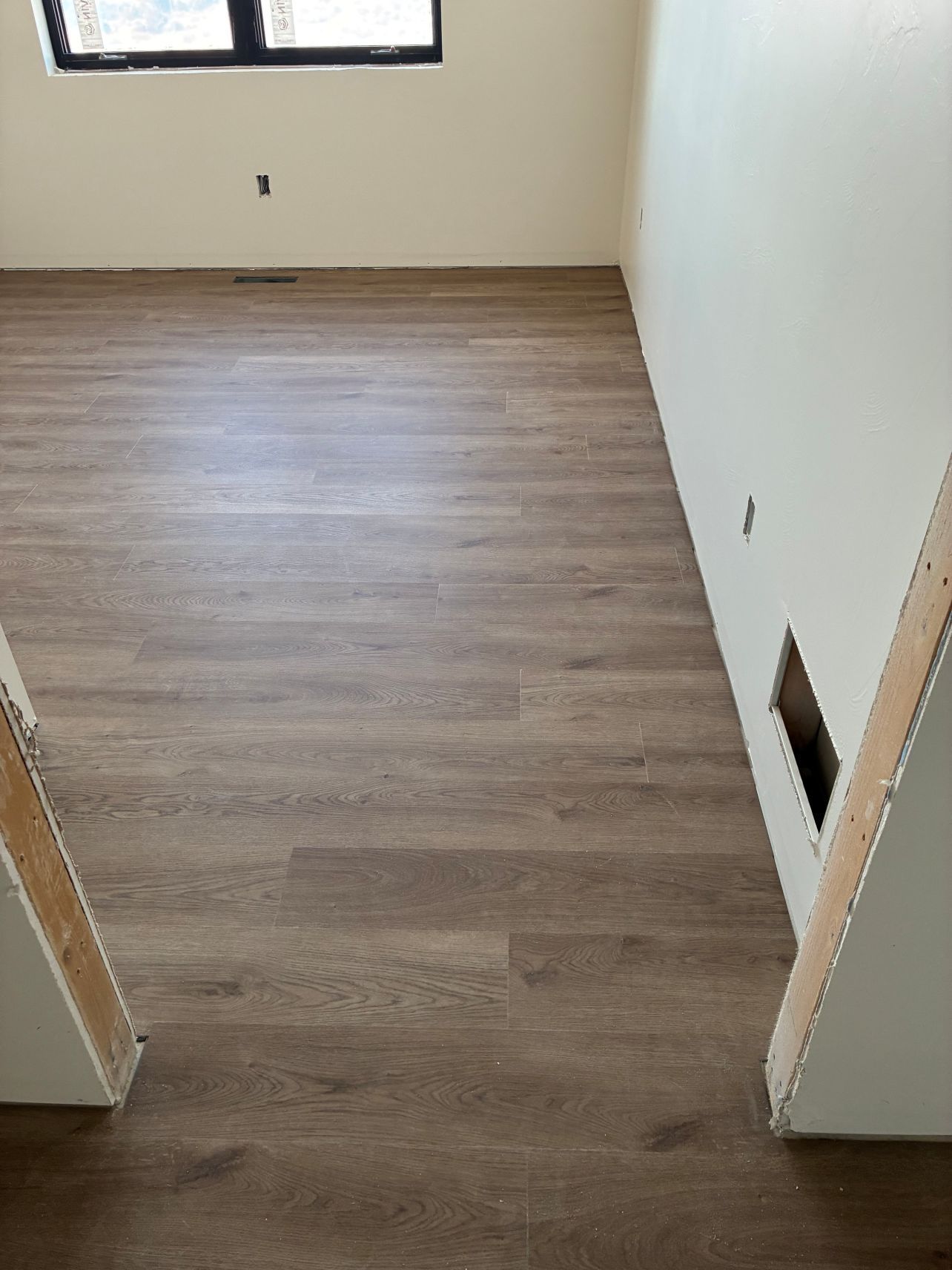 Empty room with wood-look flooring, white walls, and a window at the far end.