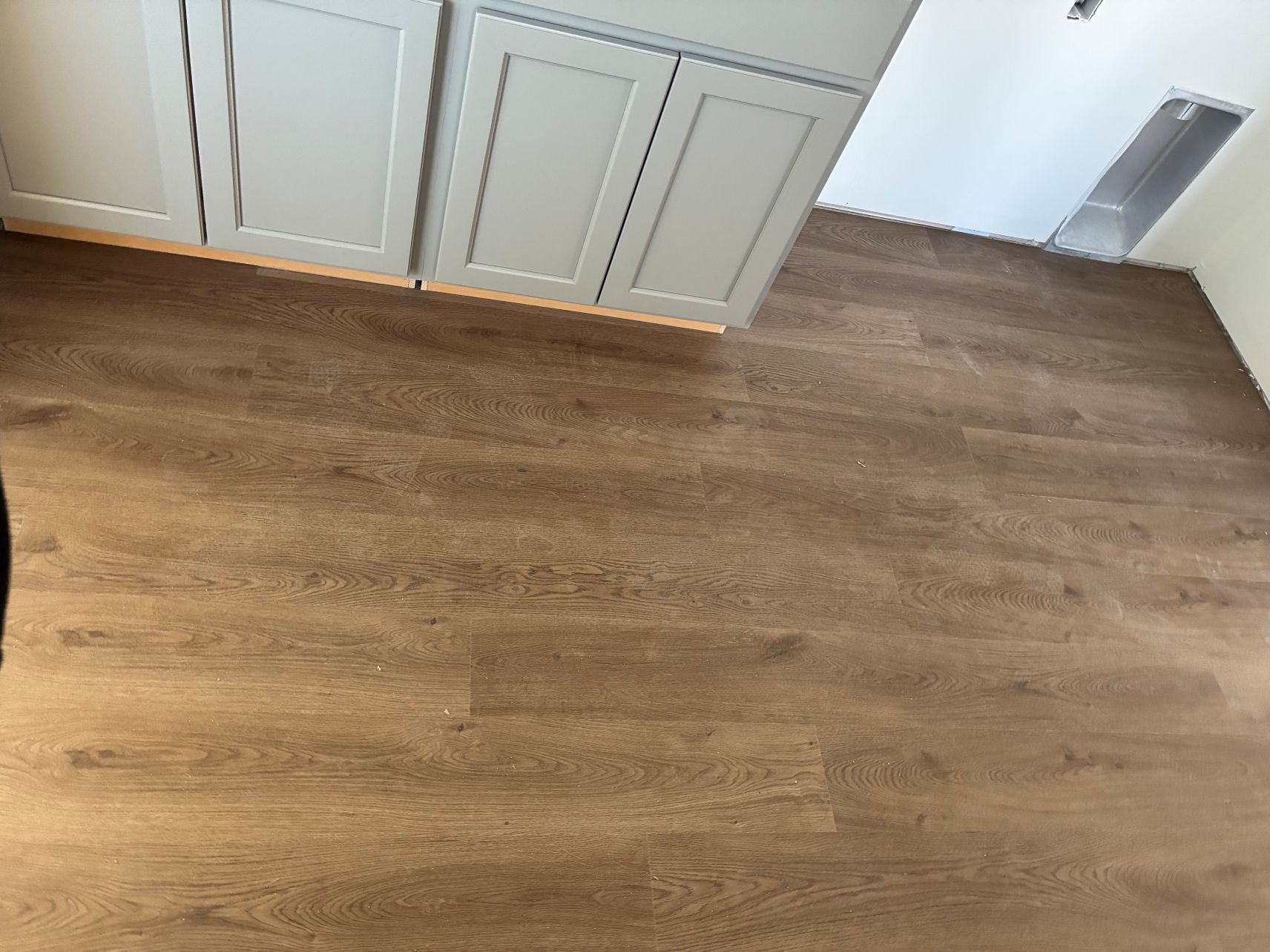 Empty room corner with wood flooring, white cabinets, and a small wall vent.
