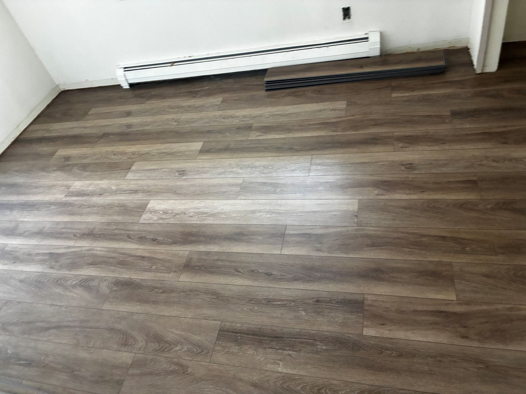 Empty room with wood flooring and a baseboard heater against a white wall.