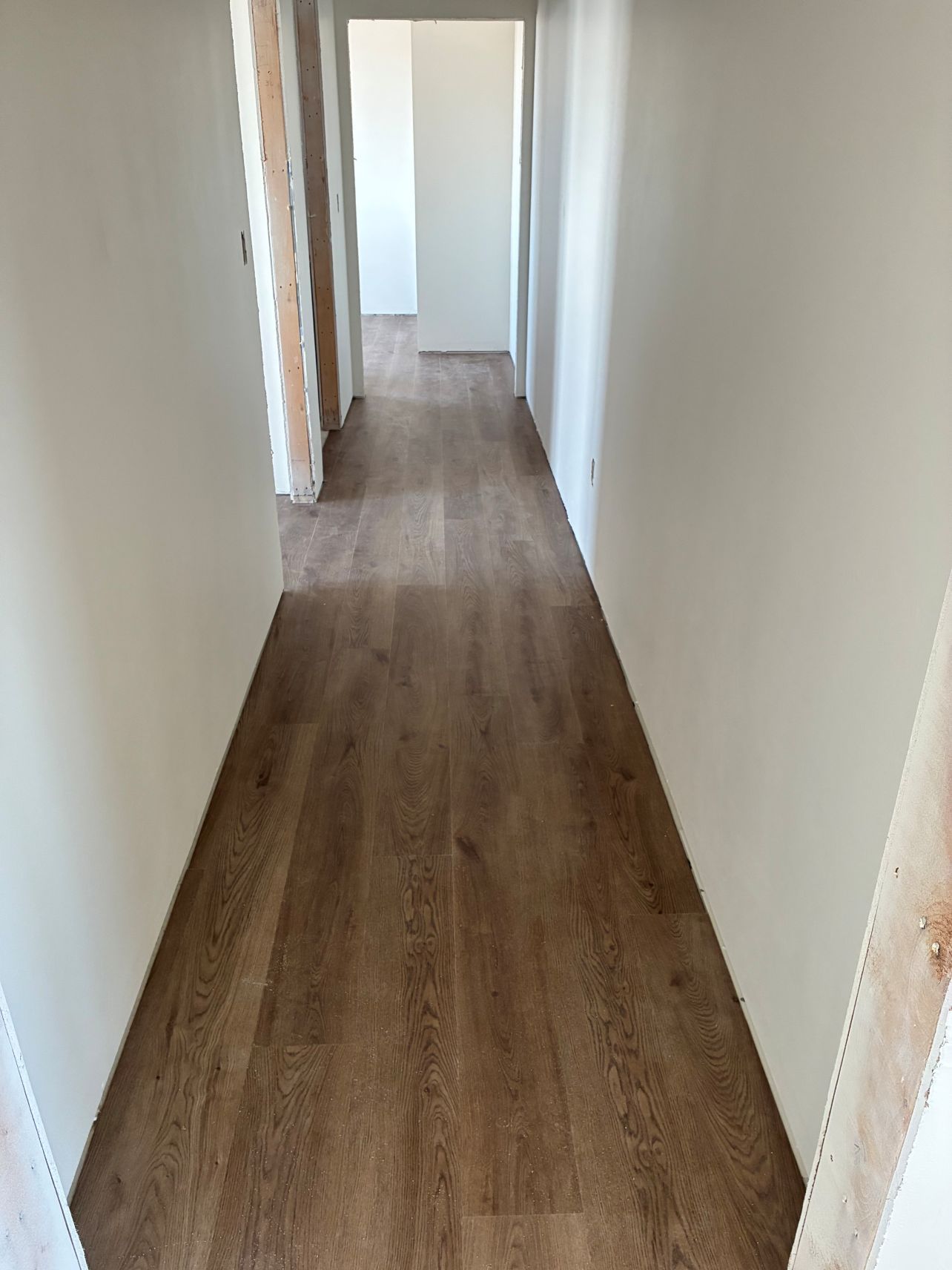 Narrow empty hallway with wood flooring and white walls, leading to a doorway at the end