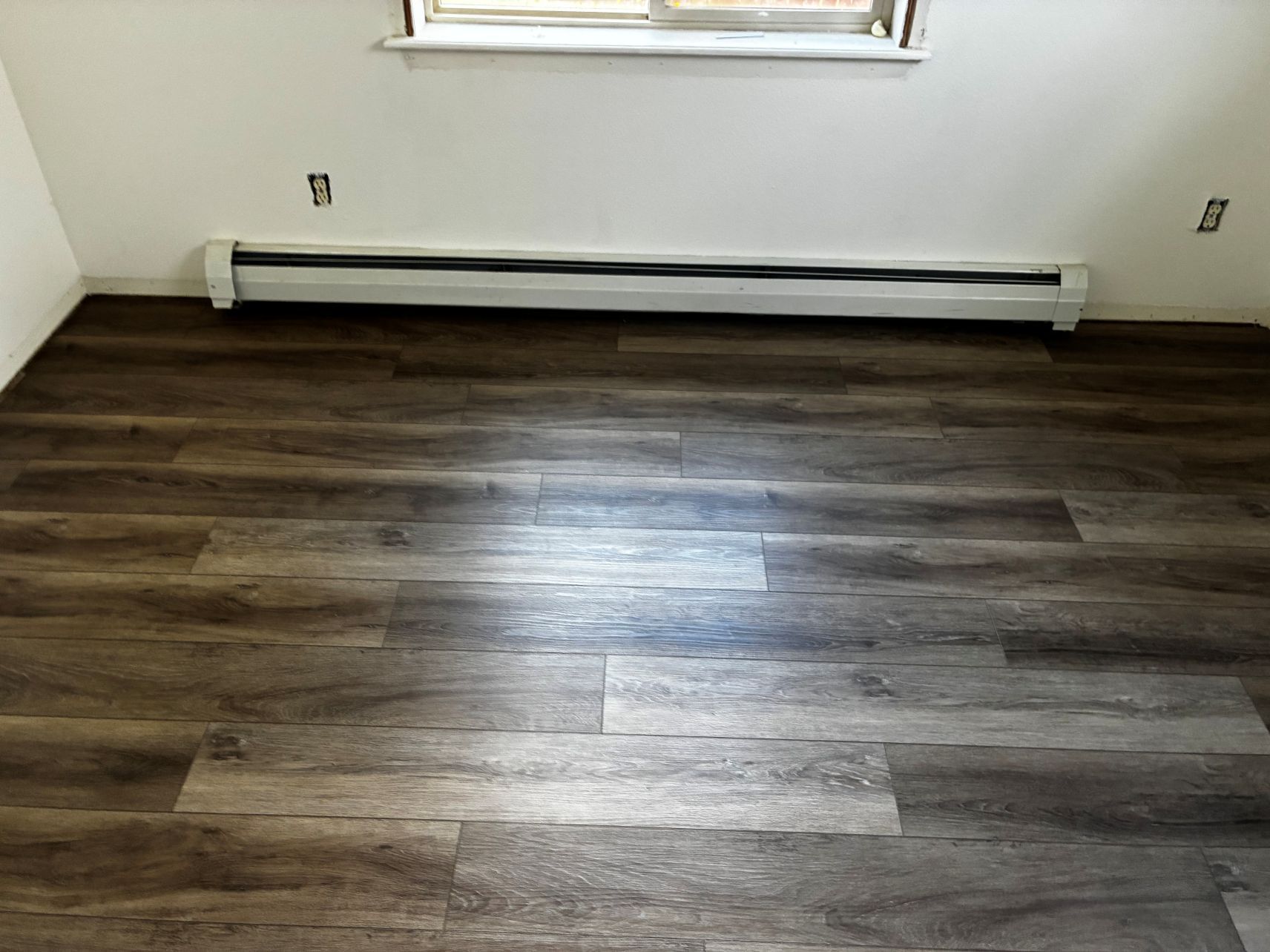 Empty room with dark wood flooring, white walls, and a window above a baseboard heater