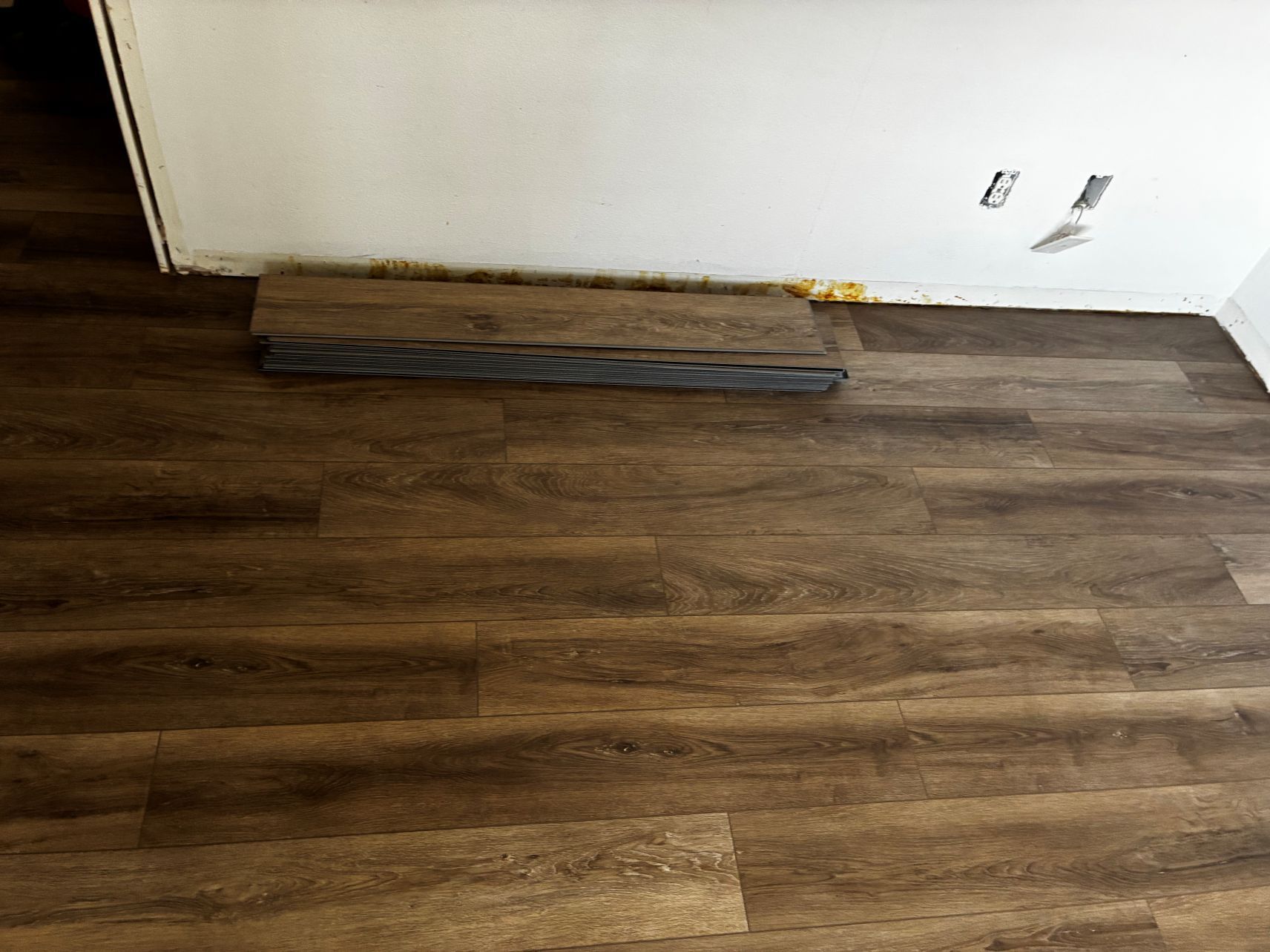 Baseboard heater against a white wall above a dark wood floor with scuffed trim paint