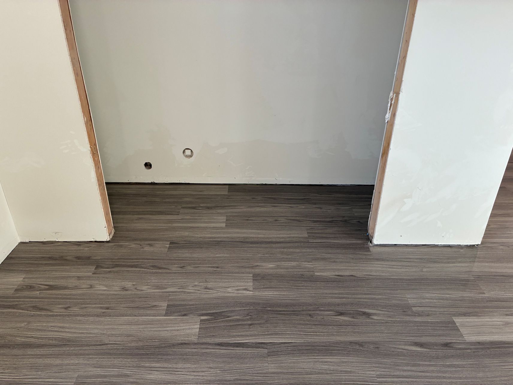 Empty room wall with white columns and dark wood flooring, with outlet openings near the baseboard.