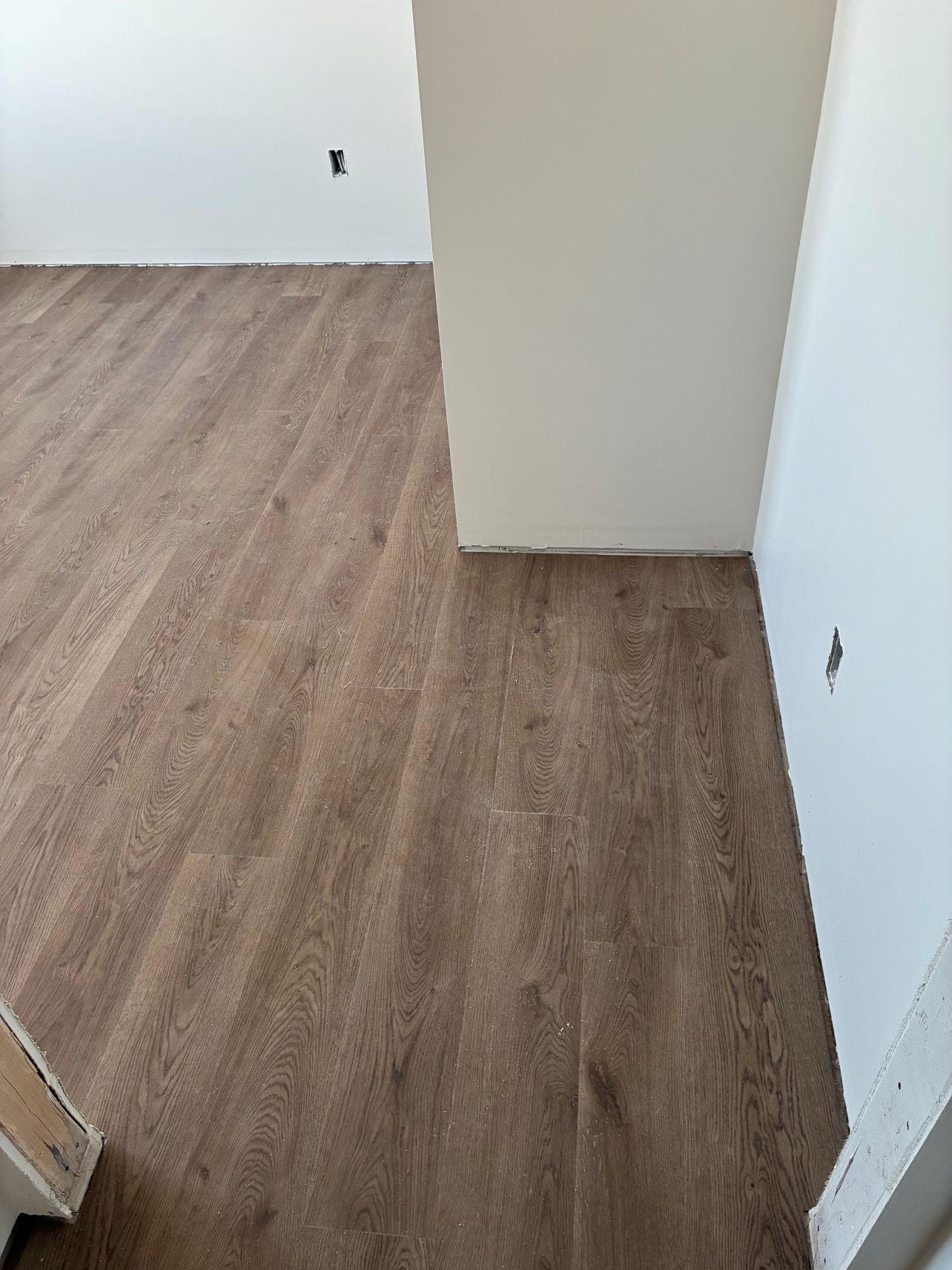 Empty room with light wood flooring and white walls, showing electrical outlets and a doorway opening.
