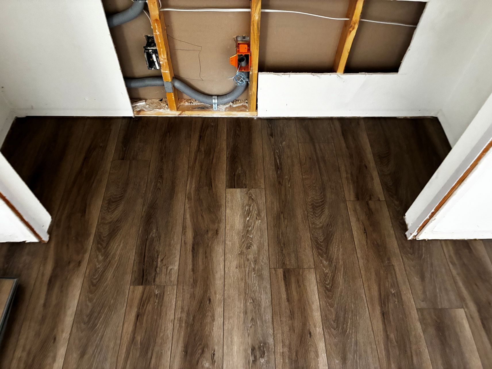 Partially finished floor with dark wood planks and exposed plumbing under open wall cavity
