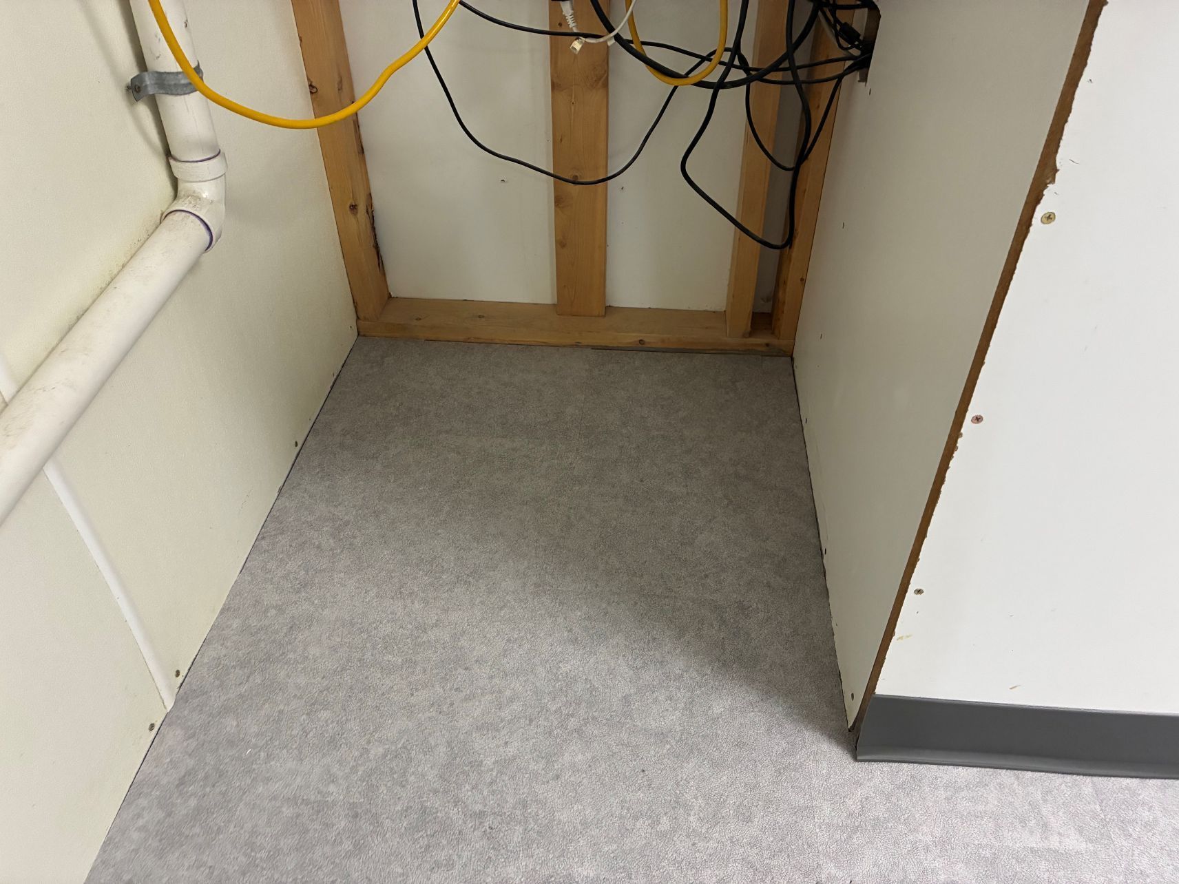 Small utility nook with gray carpet, exposed cables, and wooden framing at the back wall