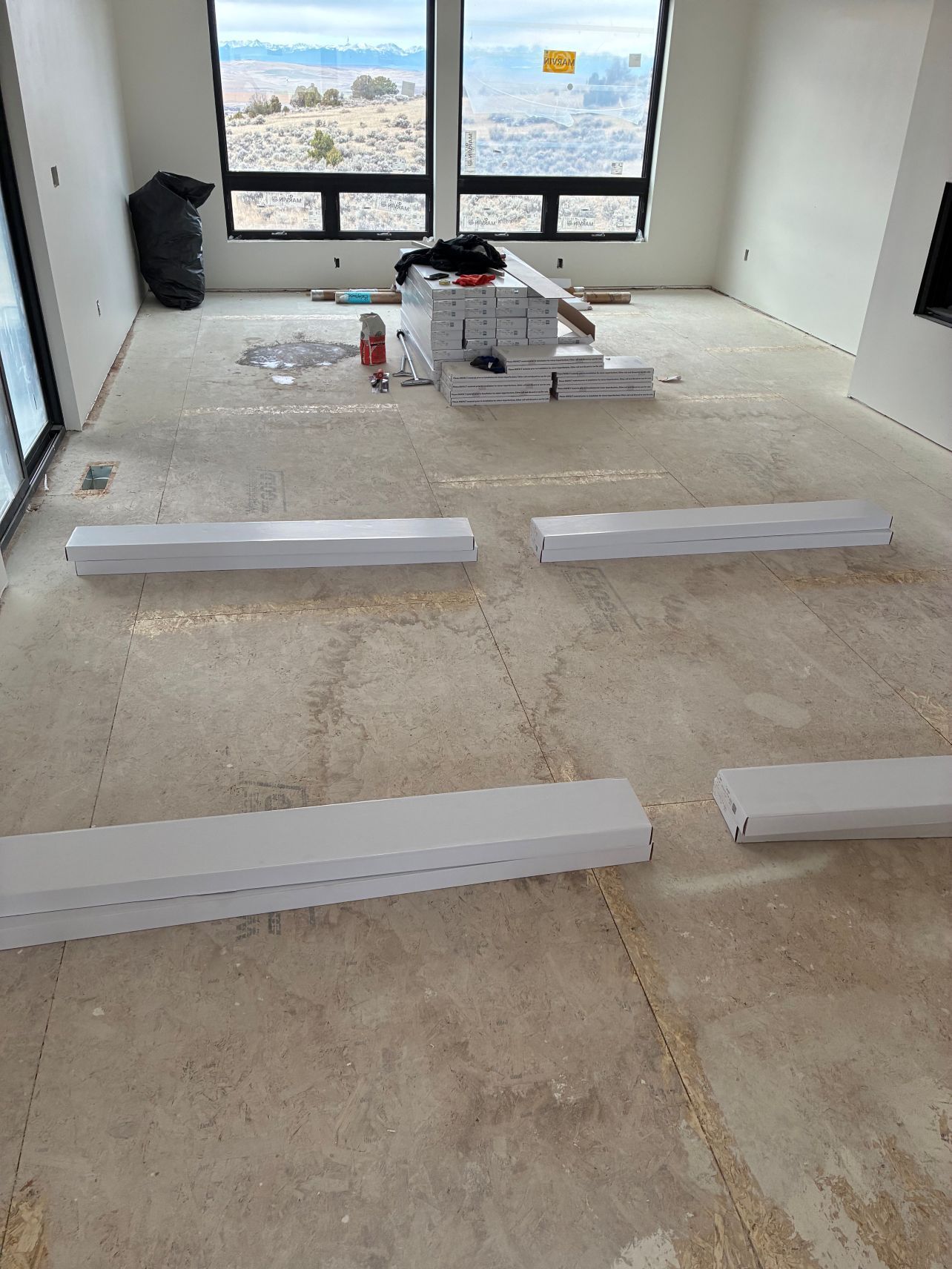 Unfinished room with white trim pieces on the floor and windows overlooking a desert landscape.
