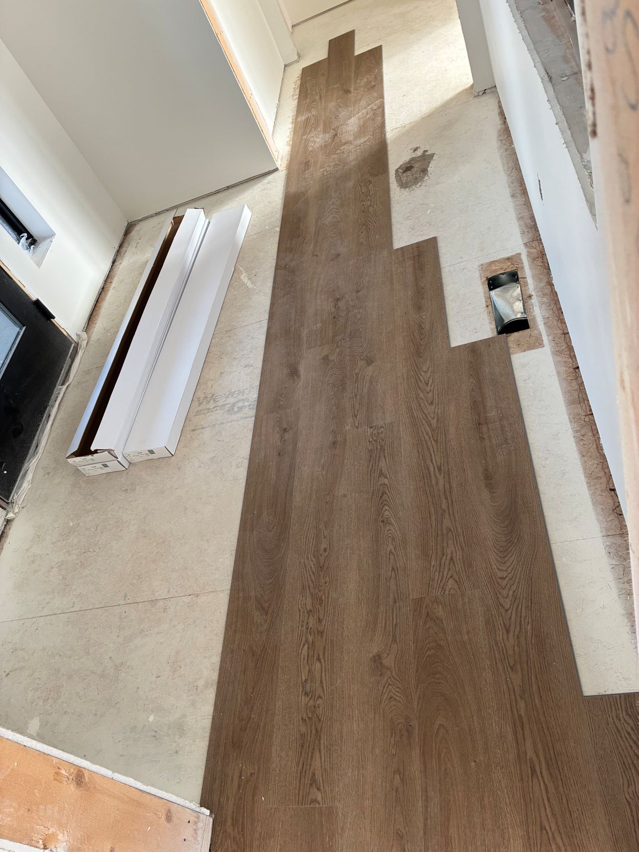 Hallway floor under renovation with wood-look flooring and exposed subfloor sections
