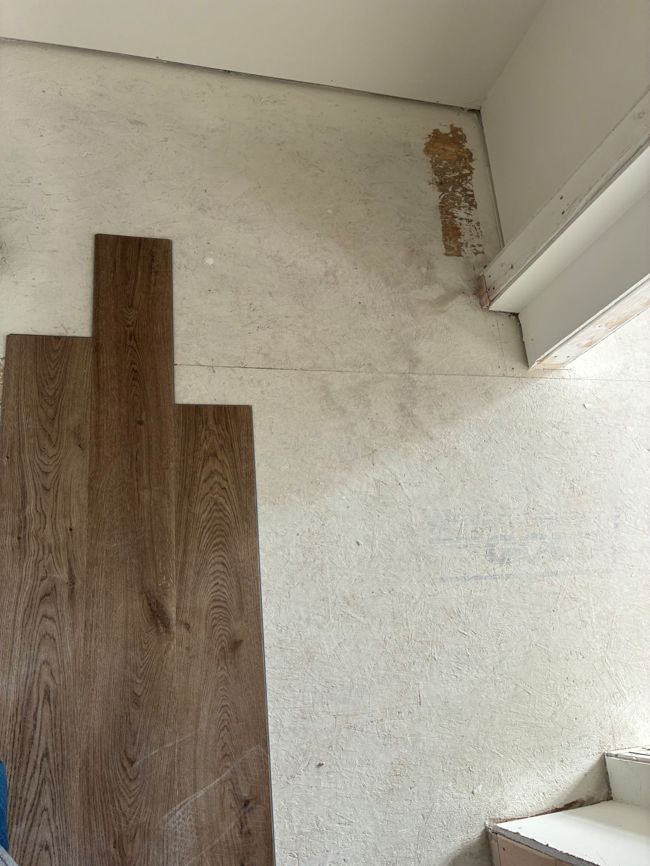 Interior wall with unfinished patching, wood flooring, and a staircase on the right.