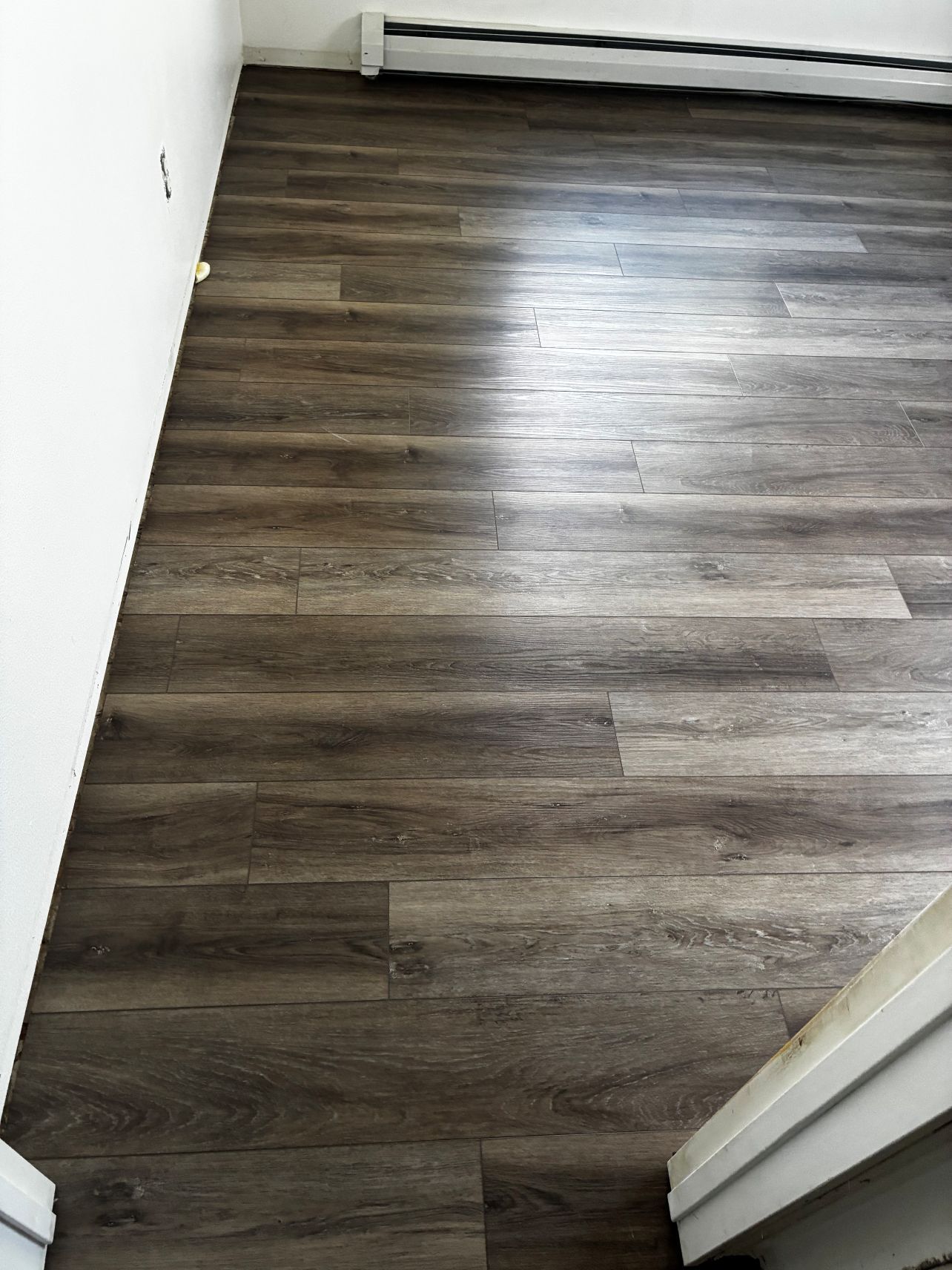 Empty room with dark wood flooring and white walls, viewed from the doorway.