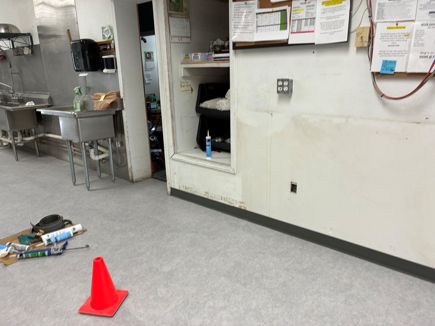 Industrial kitchen floor with spilled items and a red safety cone in front of a wall cabinet.