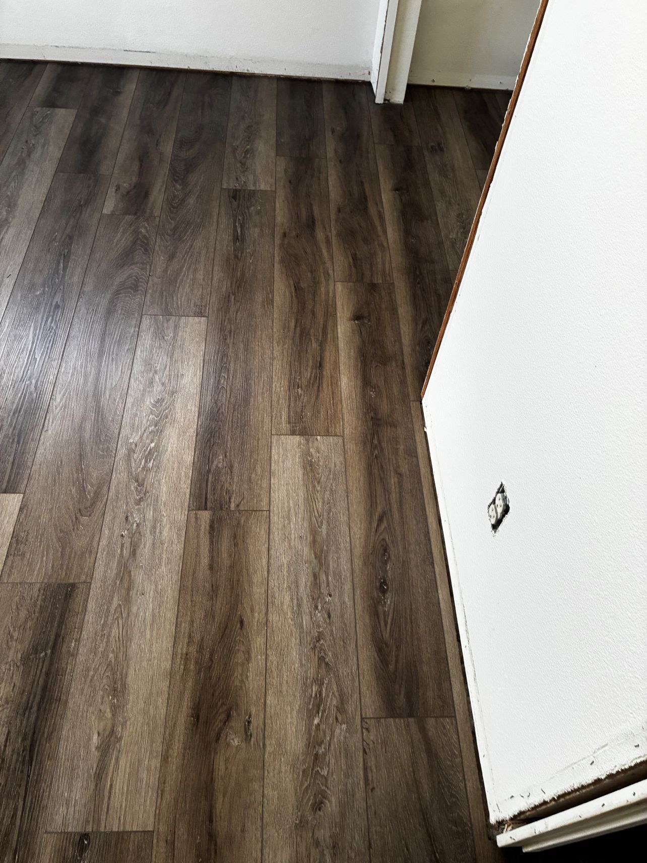 Empty room with dark wood flooring and a white wall near a doorway