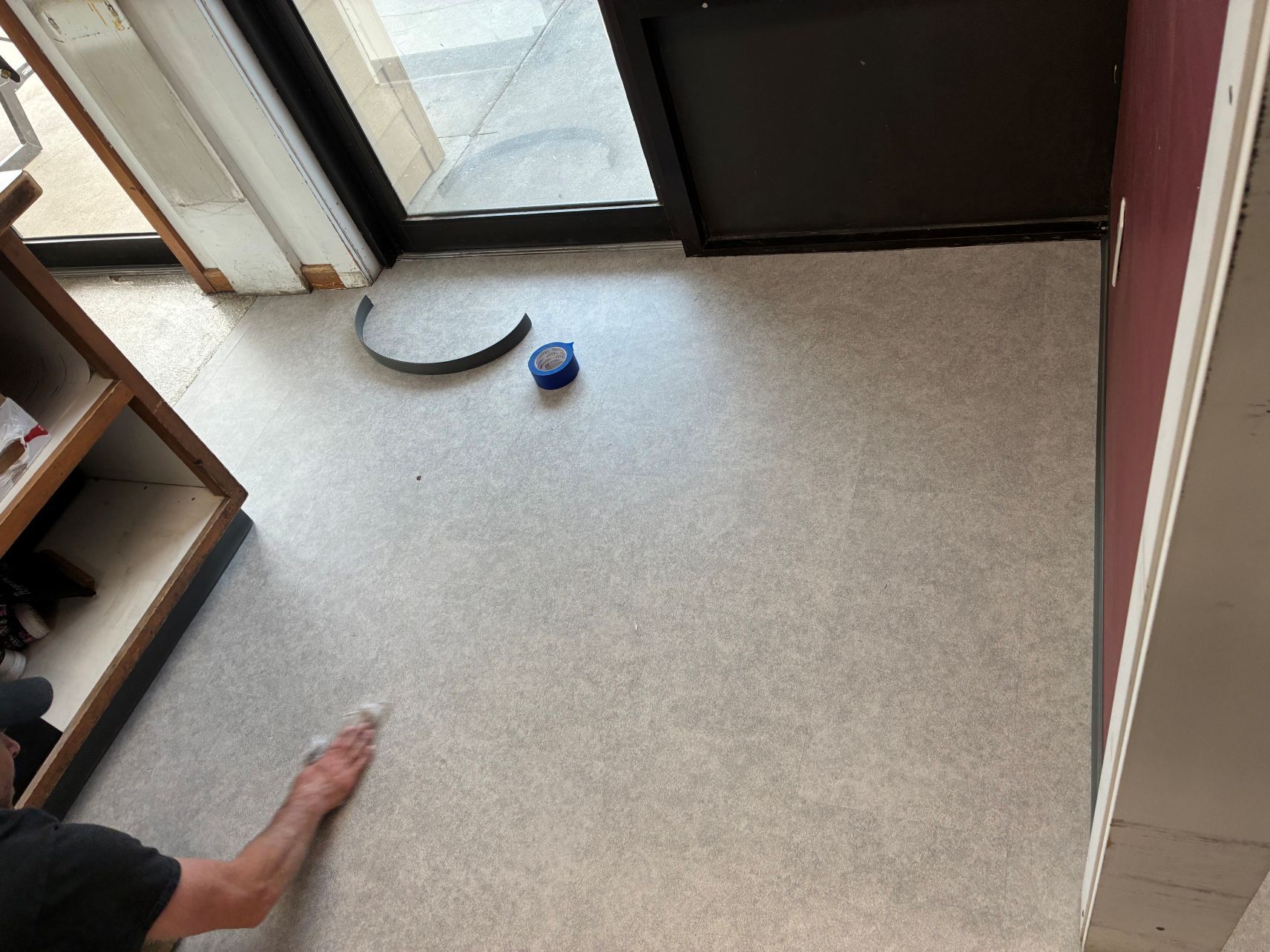 Person reaching toward a small blue object on a carpeted floor near a glass door.