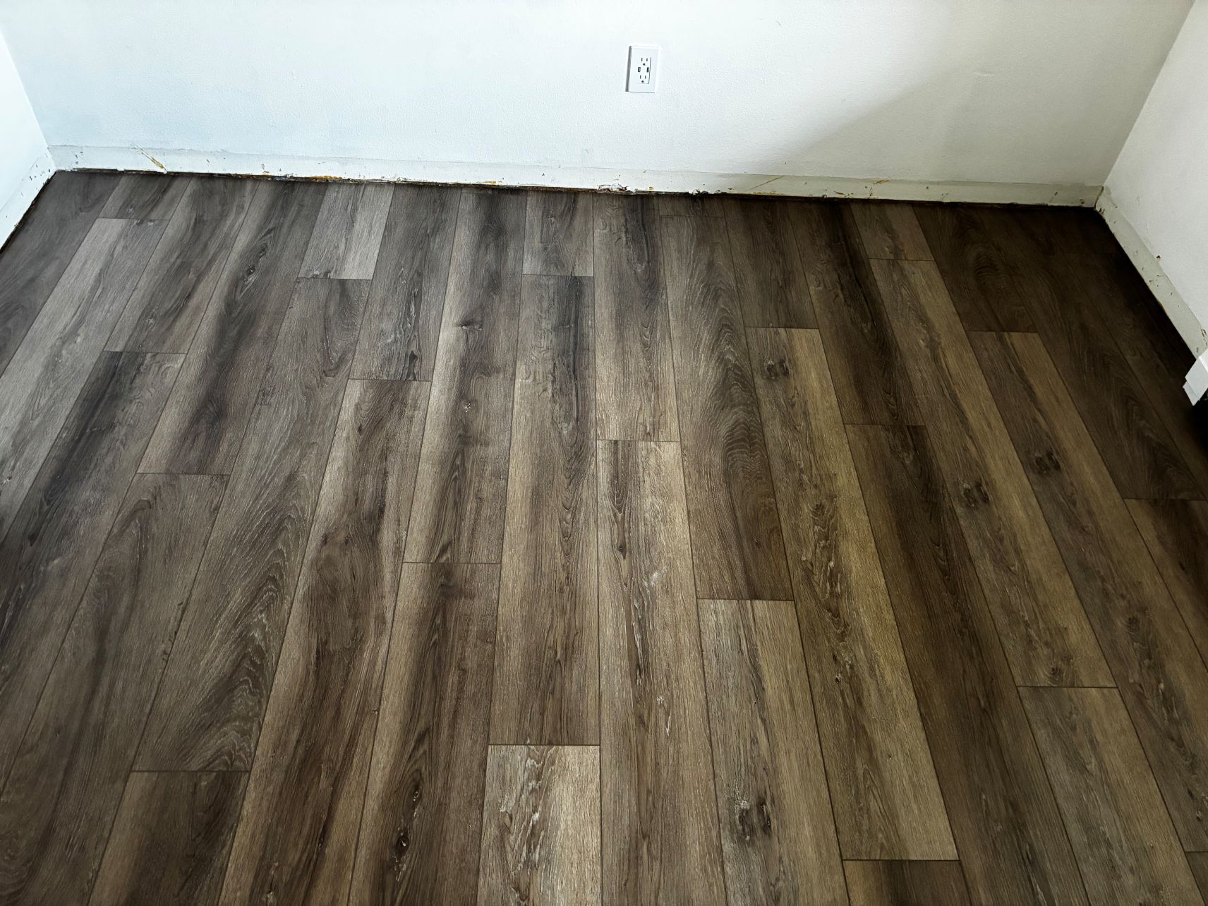 Empty room with dark wood-look flooring and white walls, viewed from a corner.