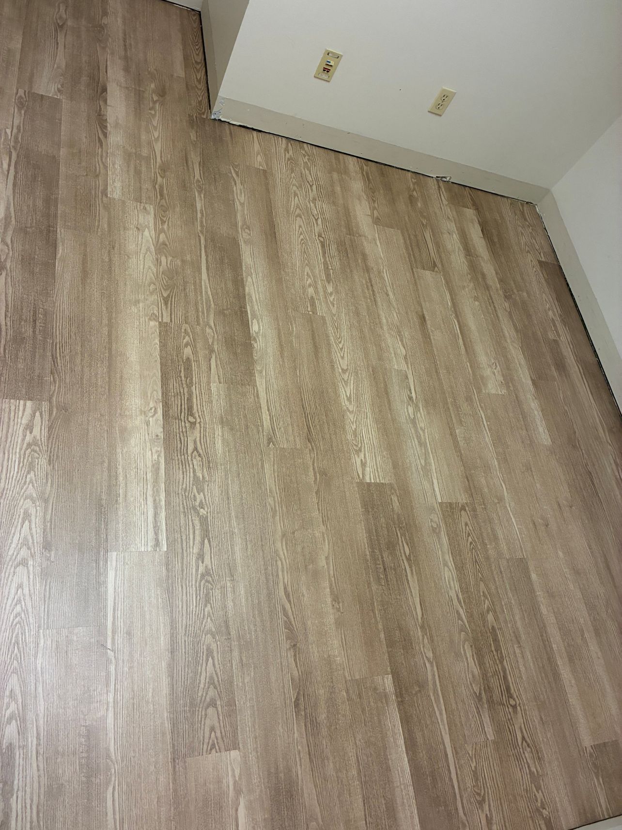 Empty room with light wood flooring and white wall with two electrical outlets.