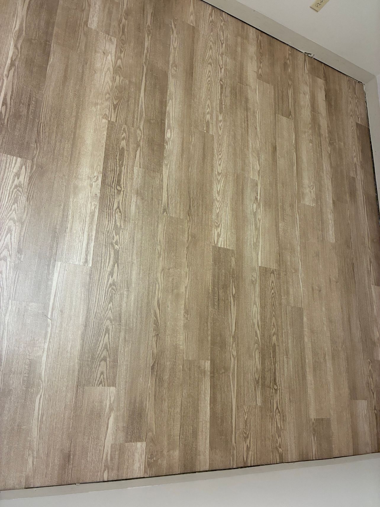 Wood-grain laminate wall panel in beige and brown tones against a white ceiling and baseboard
