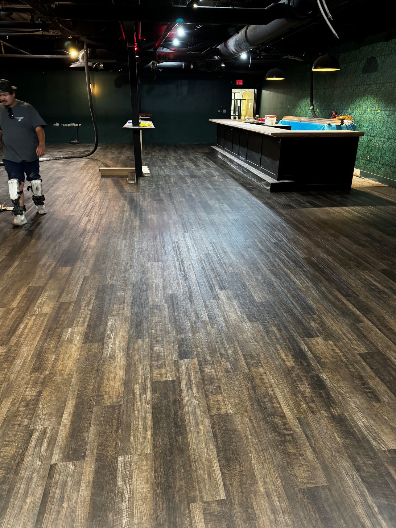 Empty entertainment room with dark wood floor, pool table, and a person standing at left