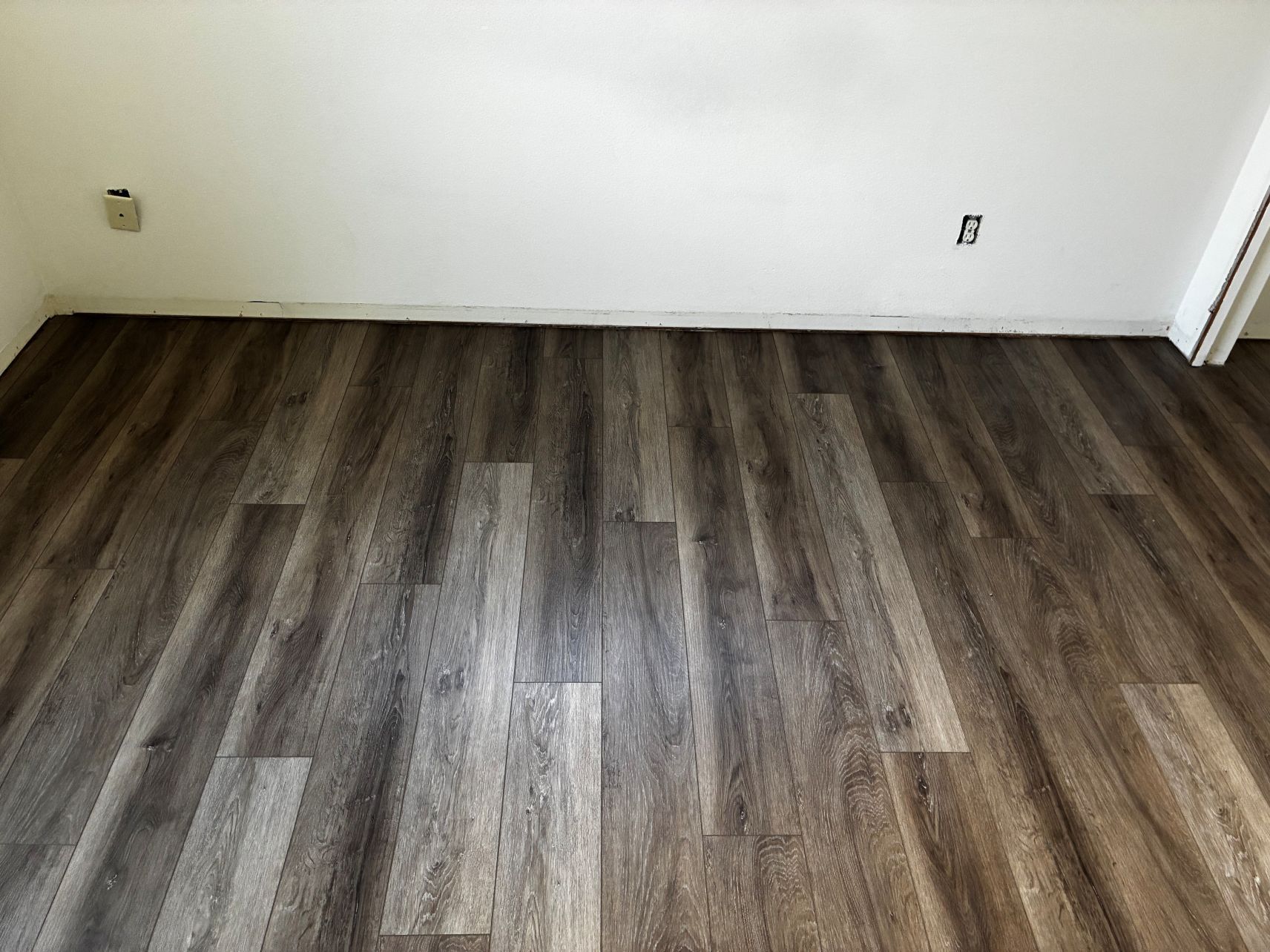 Empty room with dark wood flooring and white walls, seen from a low angle.