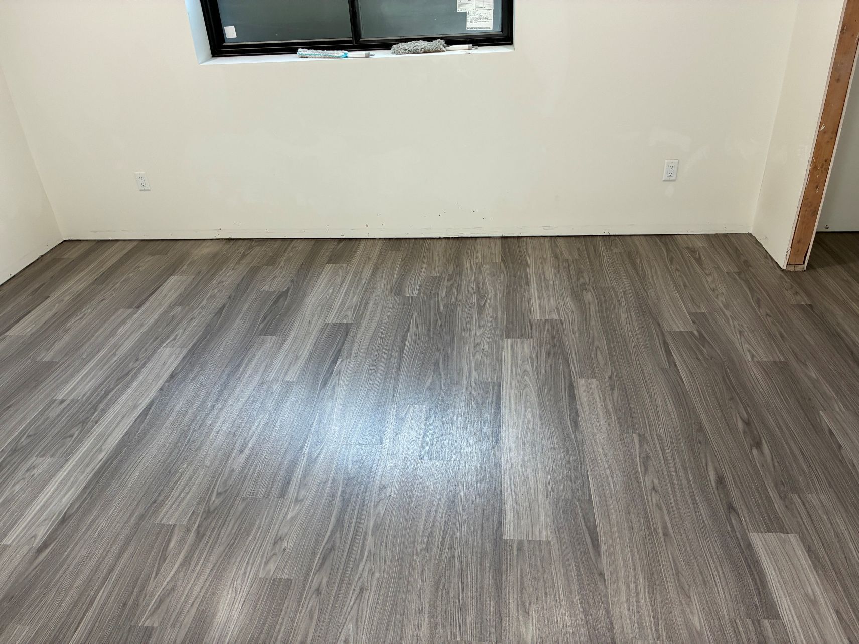 Empty room with gray wood-look flooring, beige walls, and a small window.