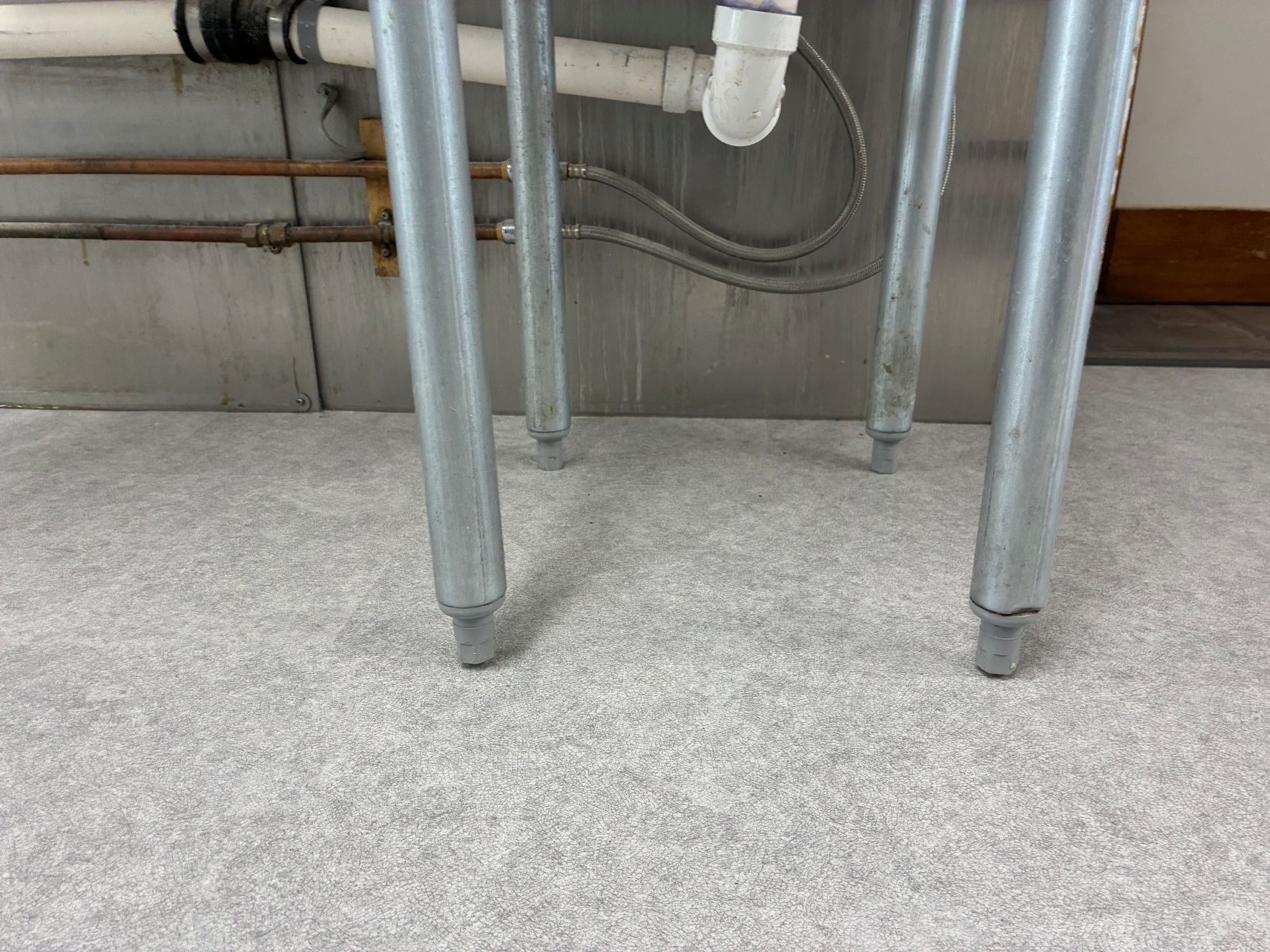 Metal table legs and plumbing pipes over a light gray carpeted floor against a wall.