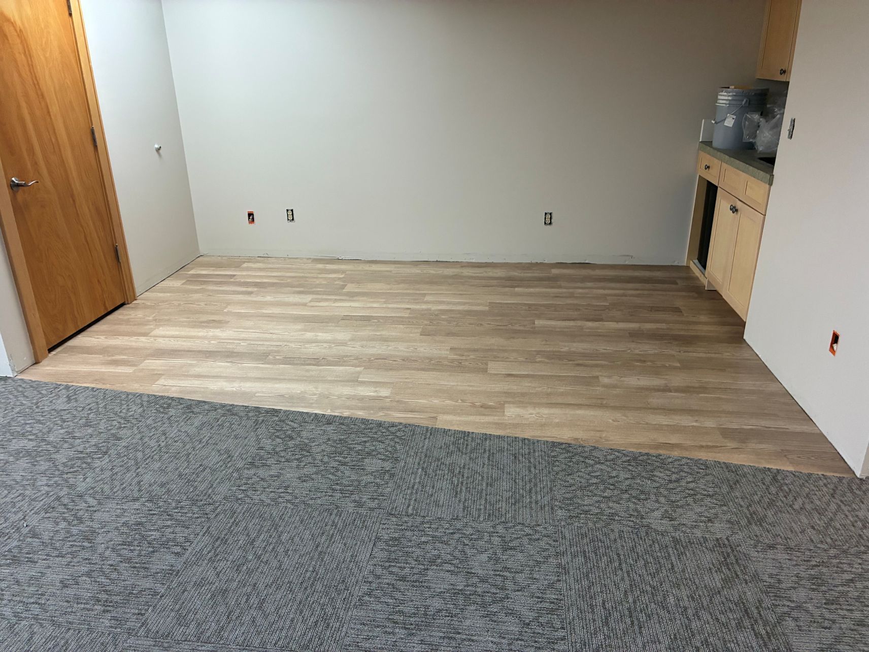Empty room with wood-look flooring, gray carpet edge, and built-in cabinets along the right wall