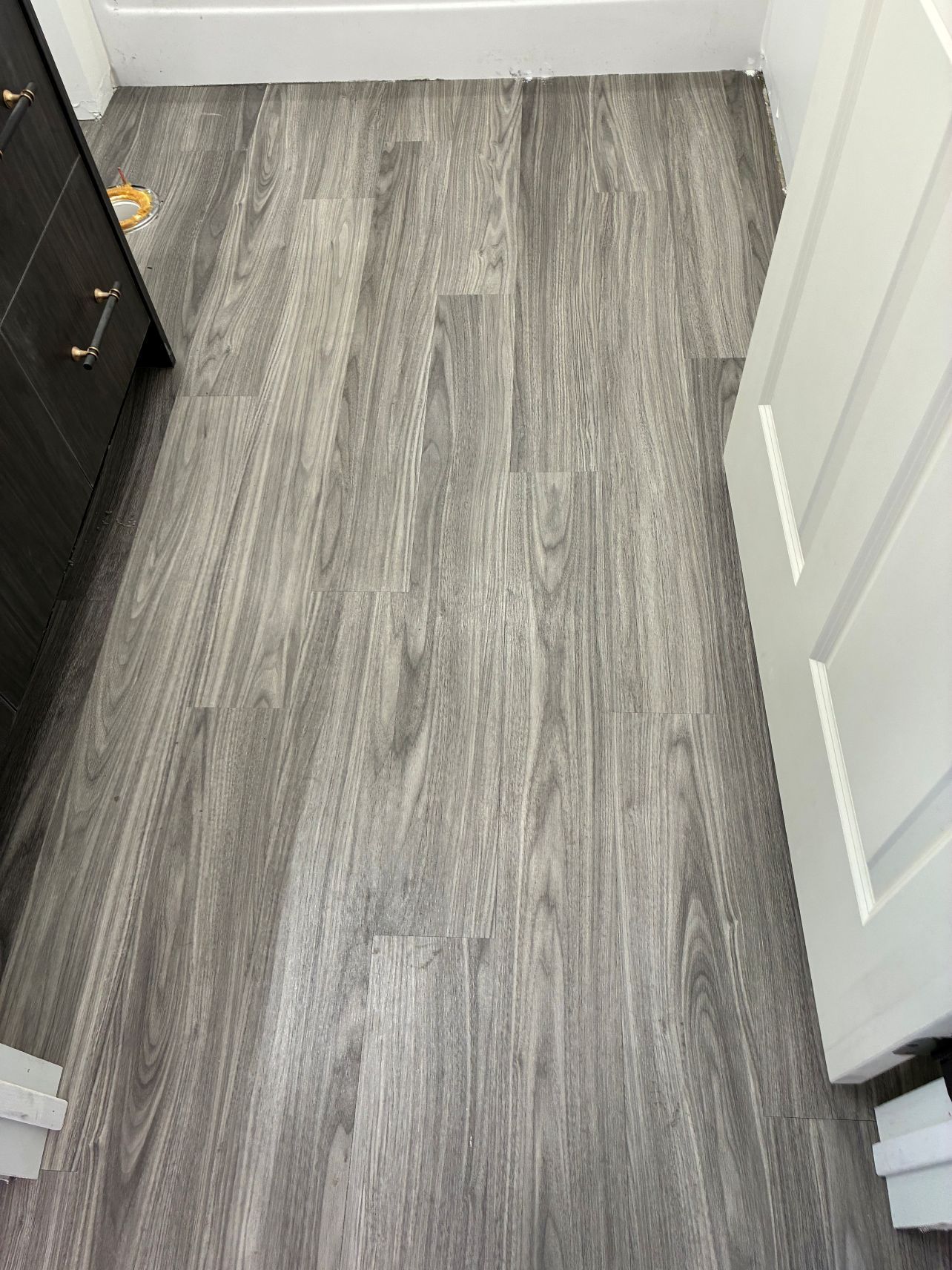 Narrow hallway with gray wood-look flooring, white walls, and a partially open white door.