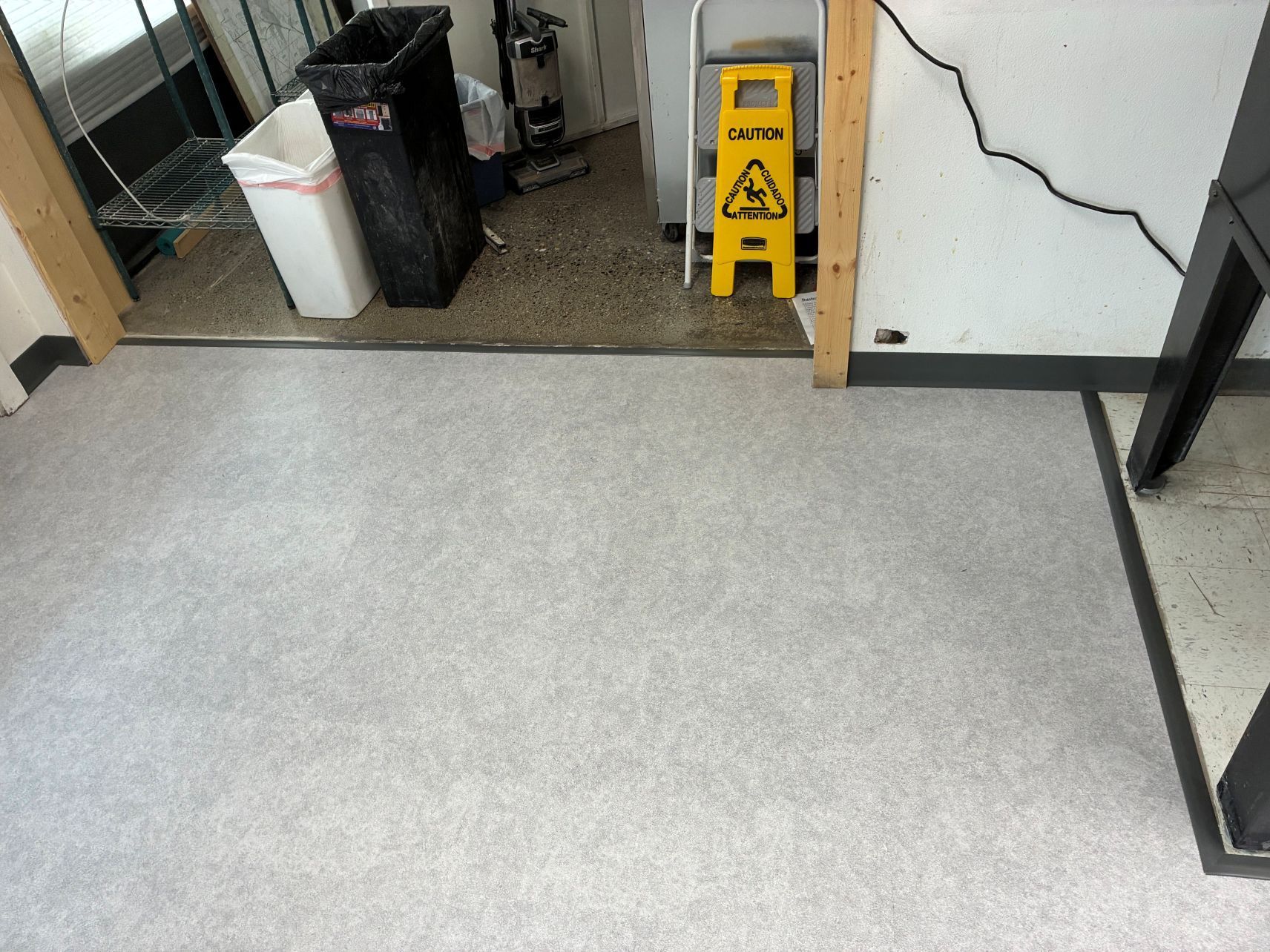Empty office floor with a yellow wet-floor sign near a doorway and a black-and-white tiled wall.