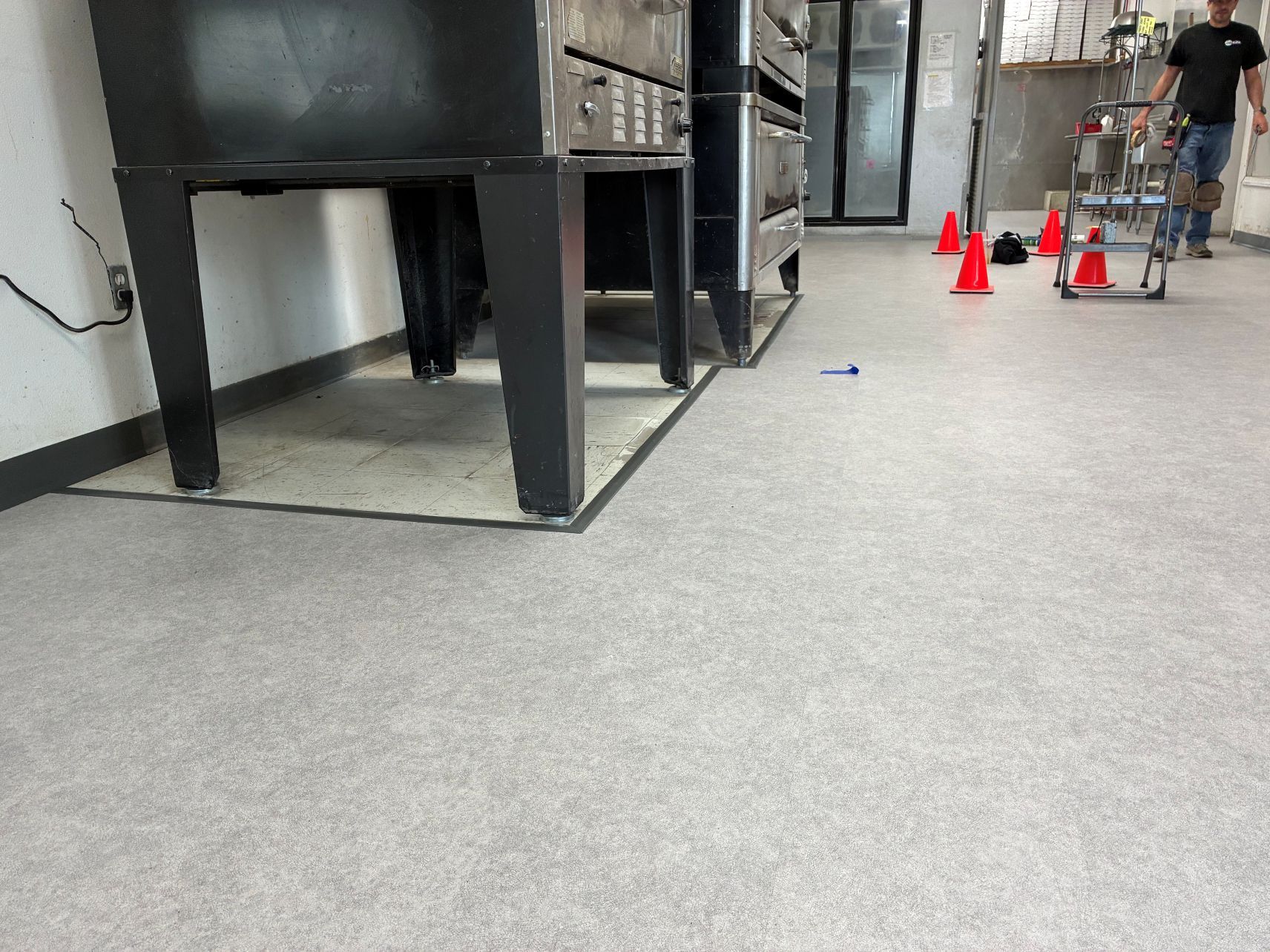 Indoor training area with cones, a cart, and a person standing near large metal equipment.