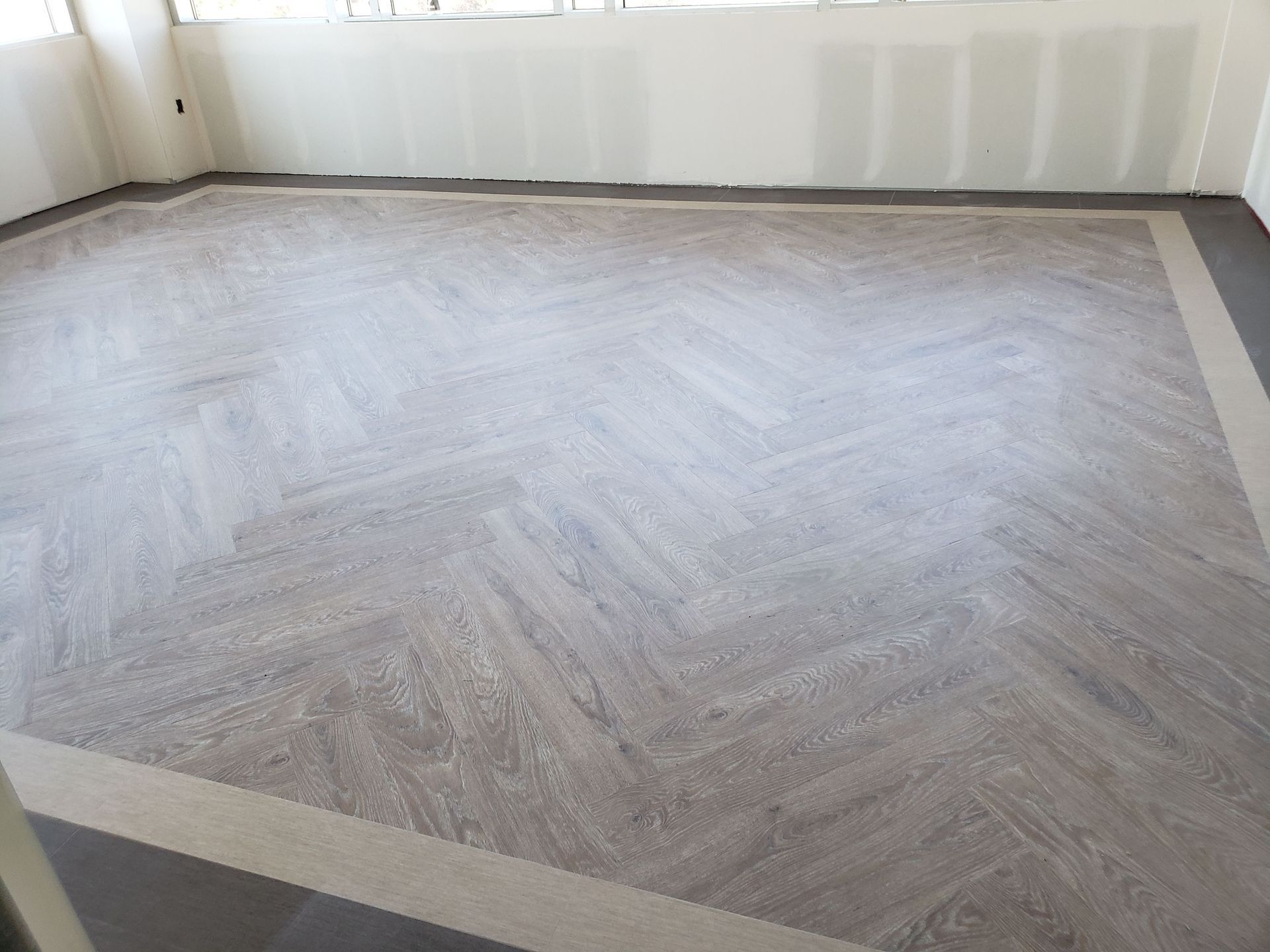 Empty room with light gray herringbone floor and white walls under renovation.