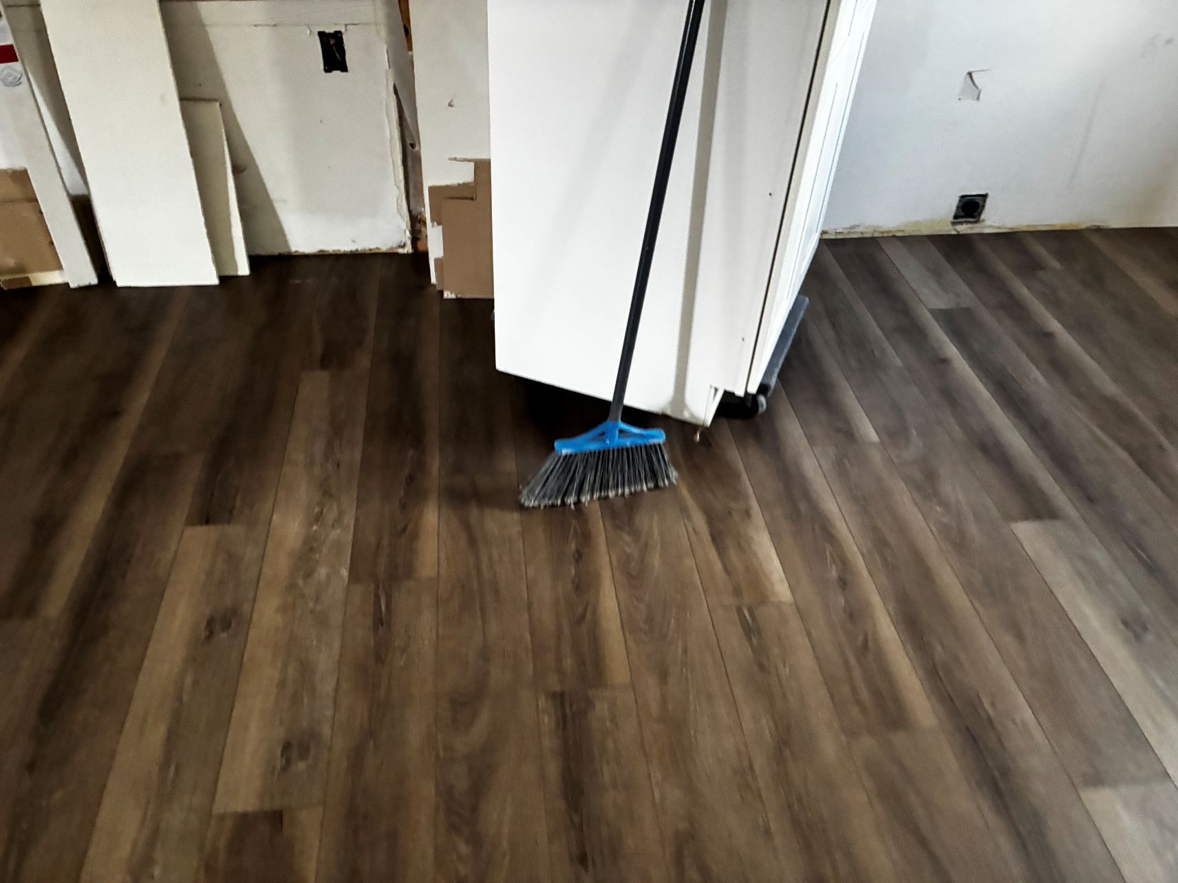 A broom leaning against a white cabinet on a dark wood floor in a room under renovation