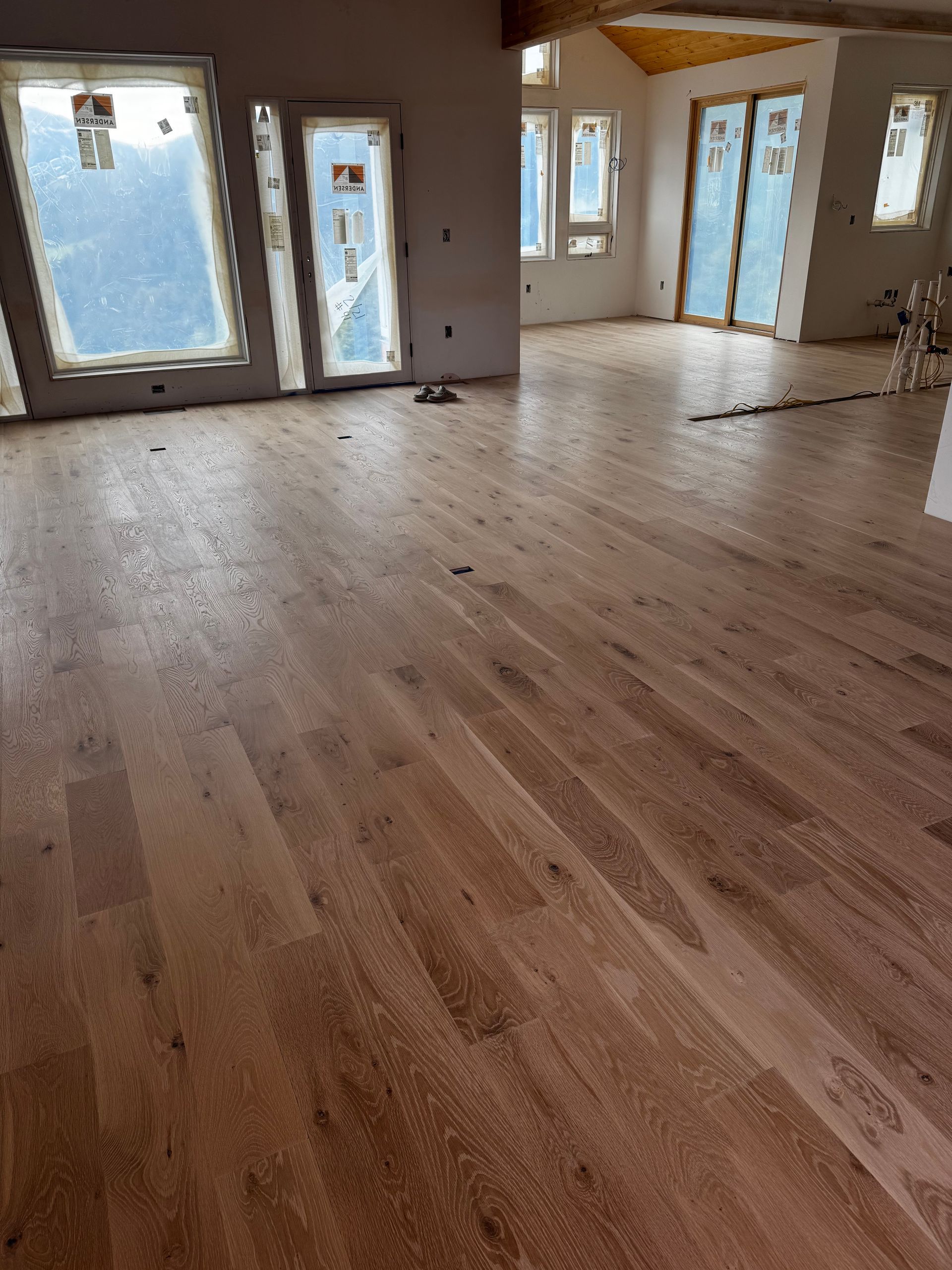 Empty room with light wood floor, large windows, and French doors letting in daylight