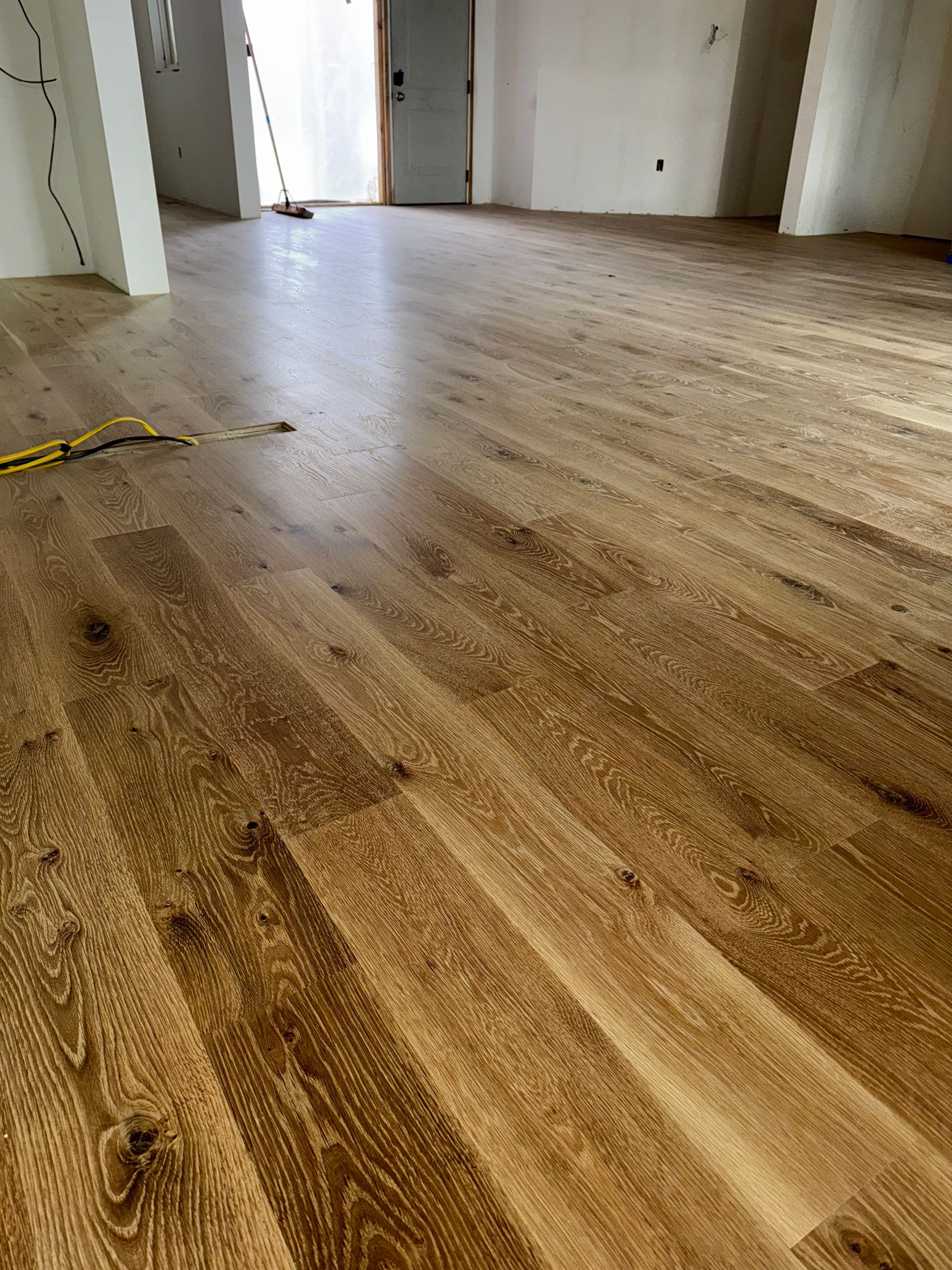 Empty room with unfinished wooden floorboards and open doors letting in bright light