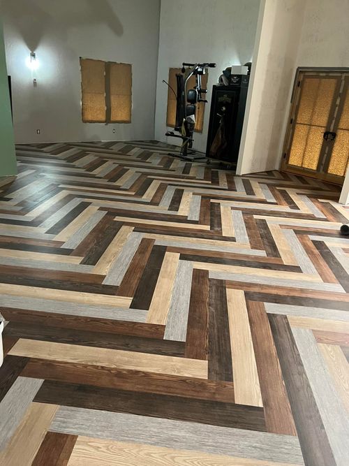 Empty room with chevron-pattern wood floor, wall mirrors, and gym equipment near the back wall
