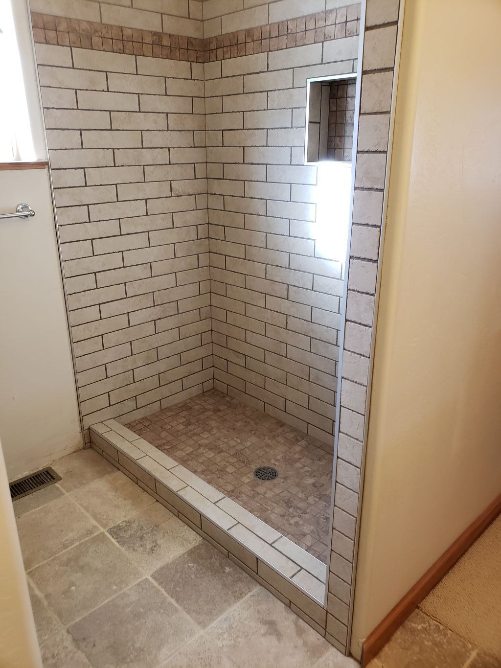 Tiled walk-in shower with a built-in bench, pebble floor, and small window.