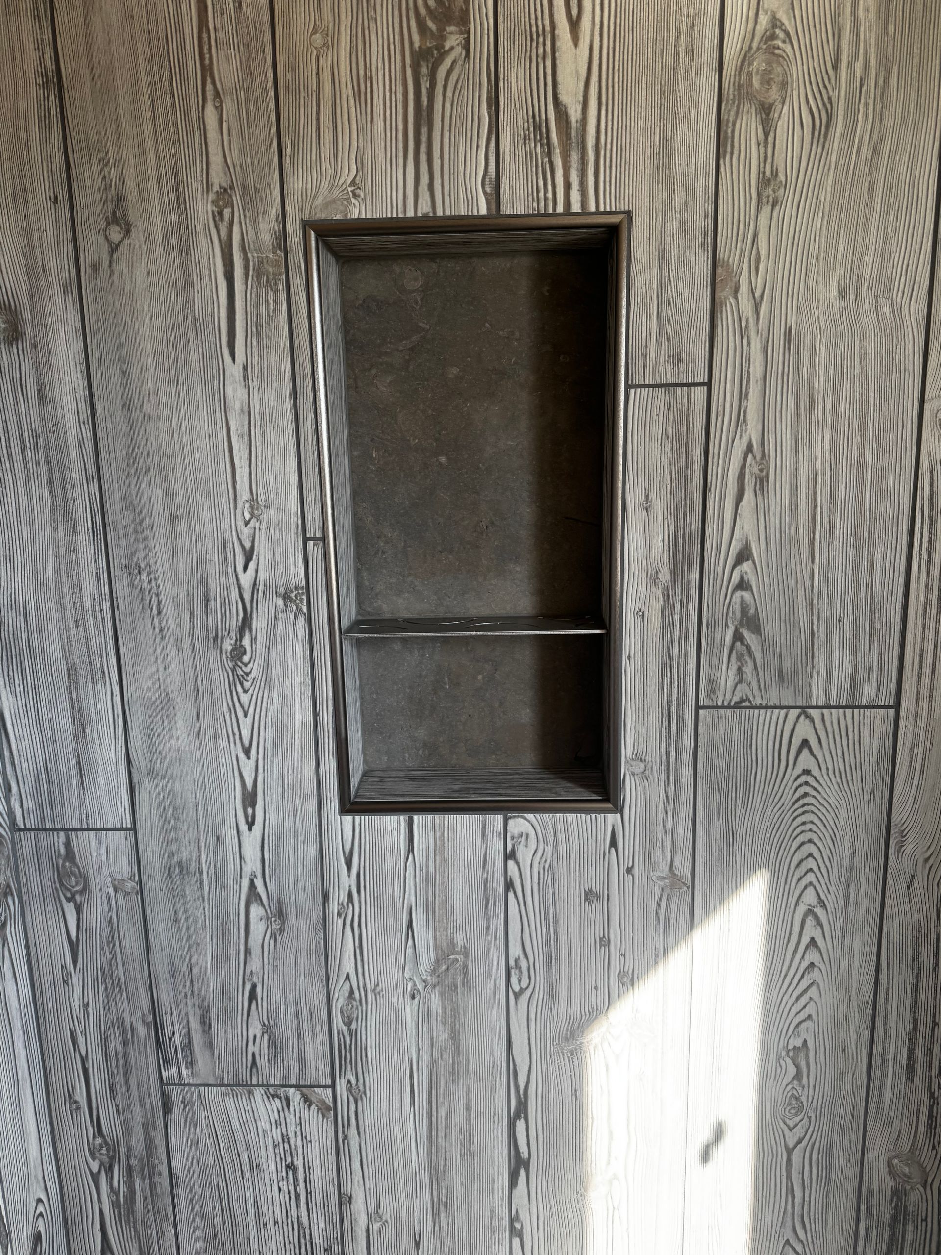 Empty recessed wall niche in gray wood-paneled wall with sunlight on the lower right side