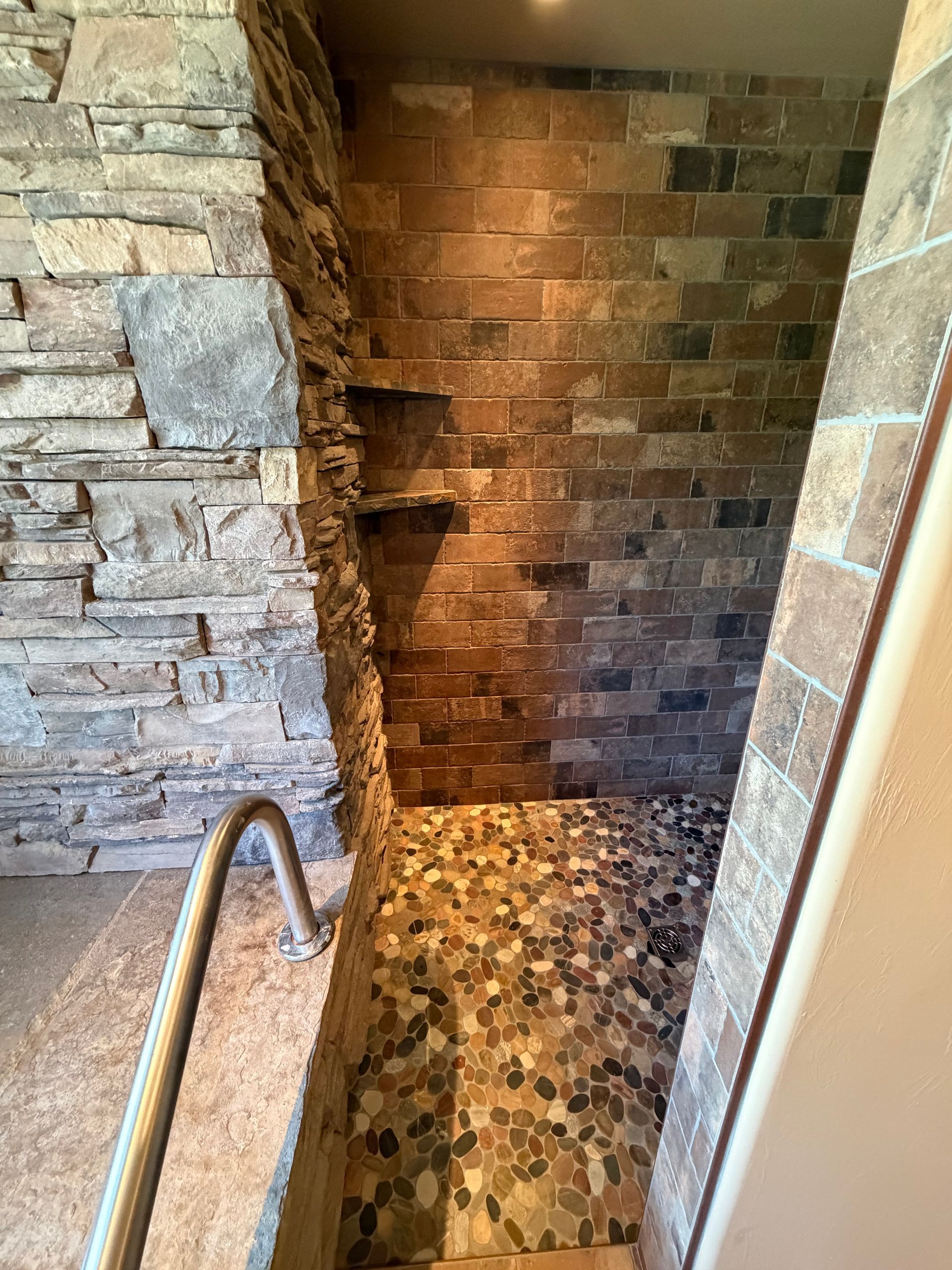 Stone-tiled shower with a mosaic floor, brick walls, and a built-in shelf niche.