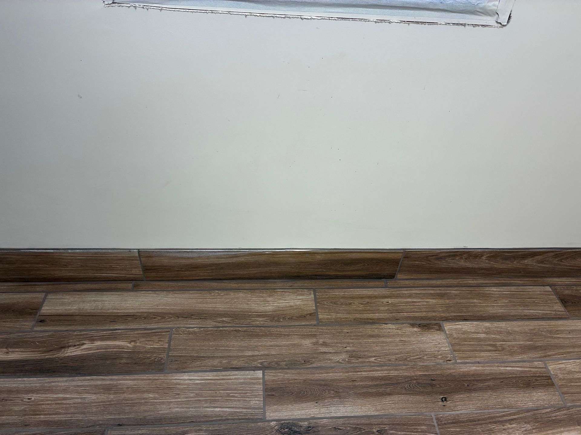 Empty white wall above brown wood-look floor with a small damaged patch near the top edge