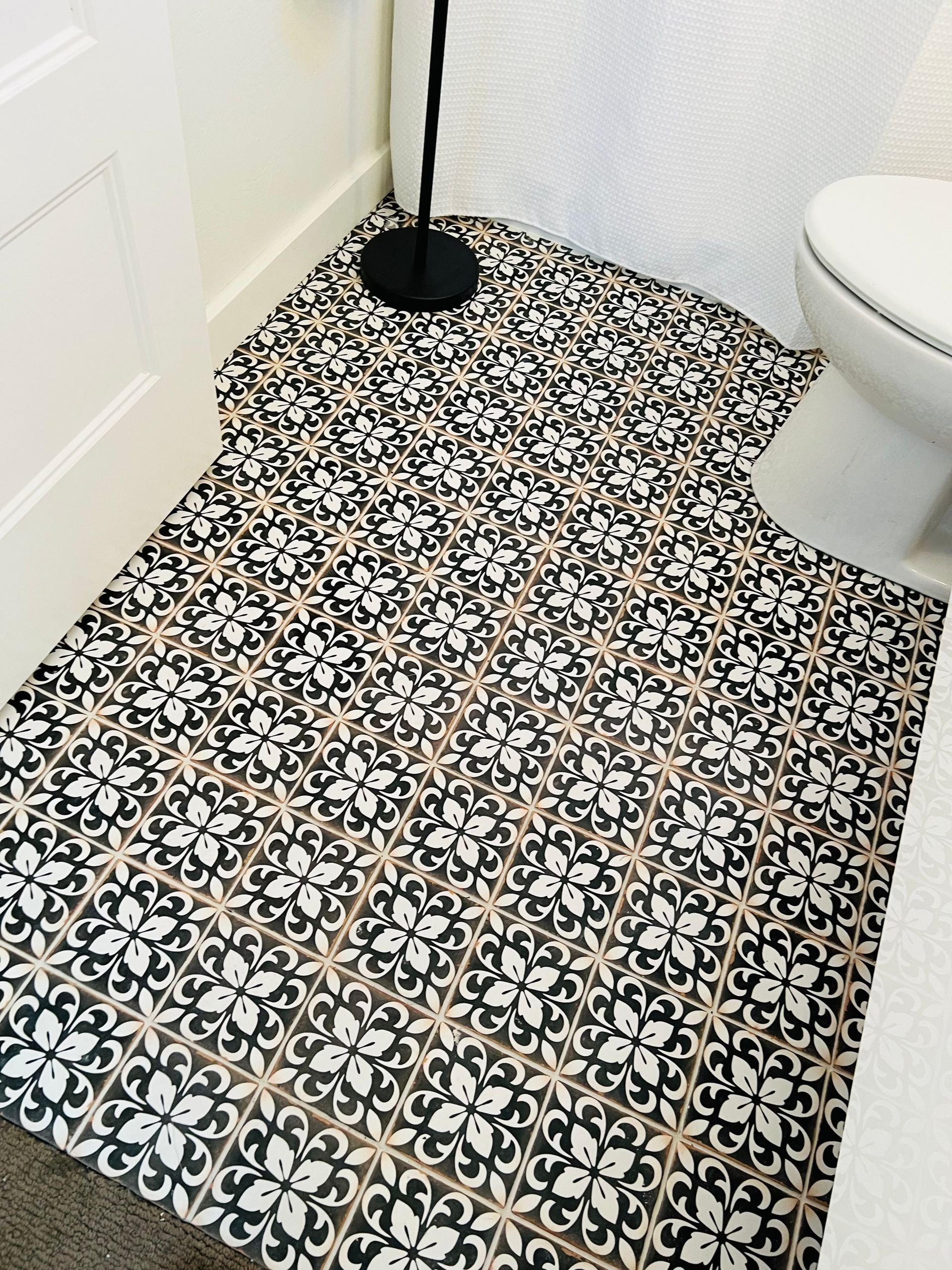 Black-and-white patterned bathroom floor with a floor lamp and partial toilet visible
