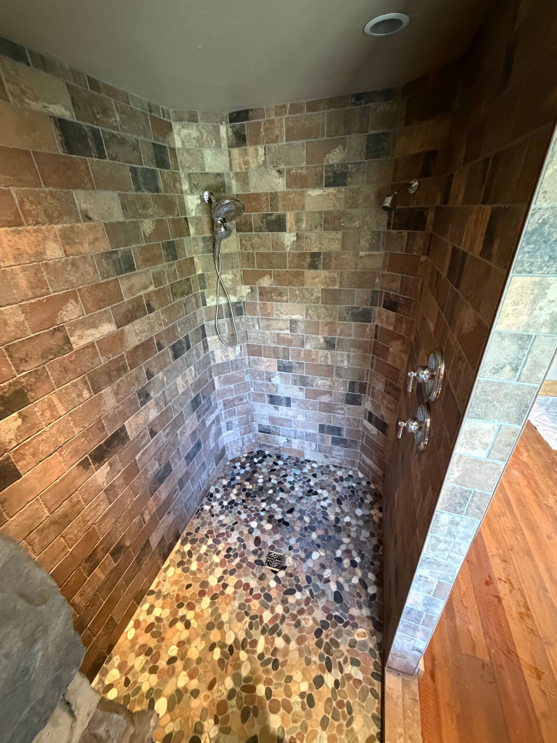Brick shower stall with a handheld showerhead and mosaic tile floor, stained and worn.
