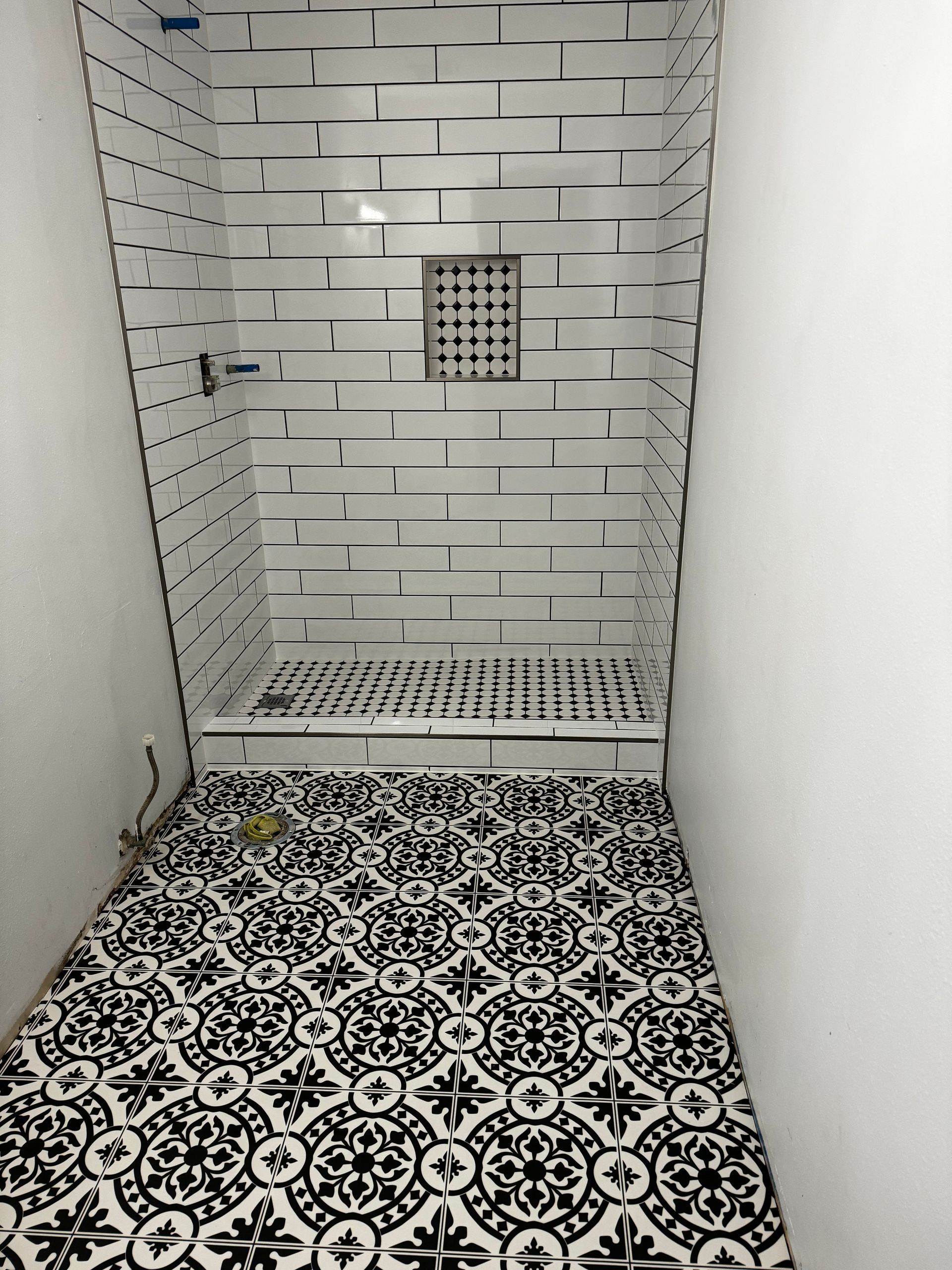 Modern tiled shower stall with a floor drain and patterned black-and-white floor tile