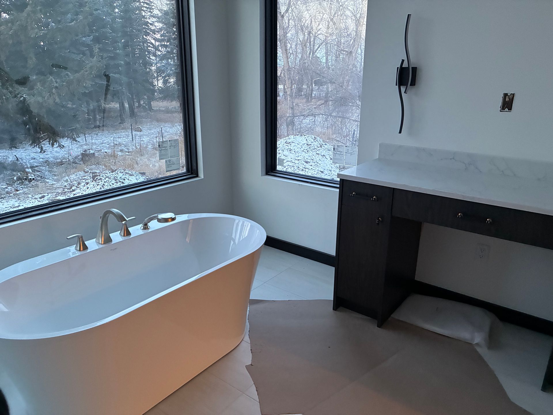 Modern bathroom with a freestanding tub, black vanity, and large windows overlooking a snowy view